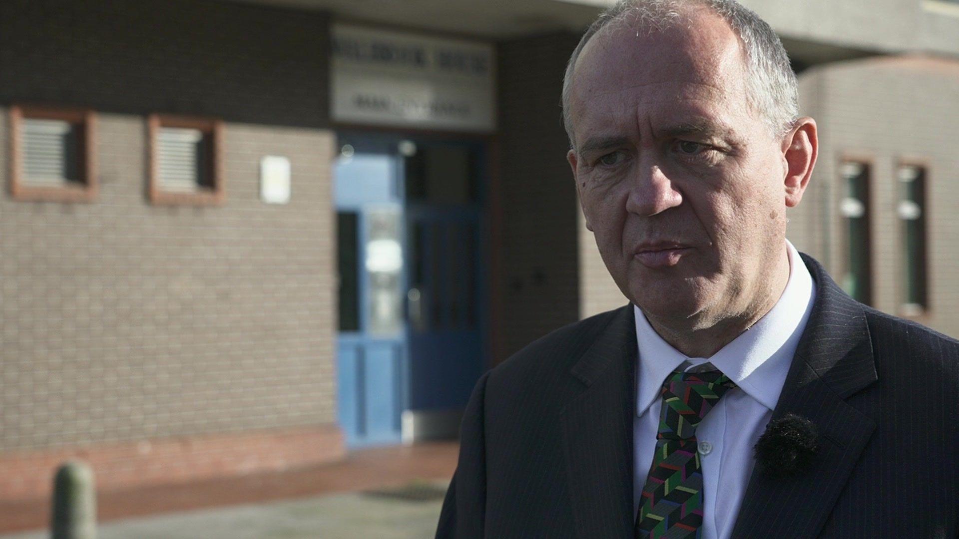 Arnold Tarling, a man with short grey hair in a black suit jacket and white shirt with a patterned green tie. he is stood outside the entrance to Walbrook House in Edmonton - an LPS building