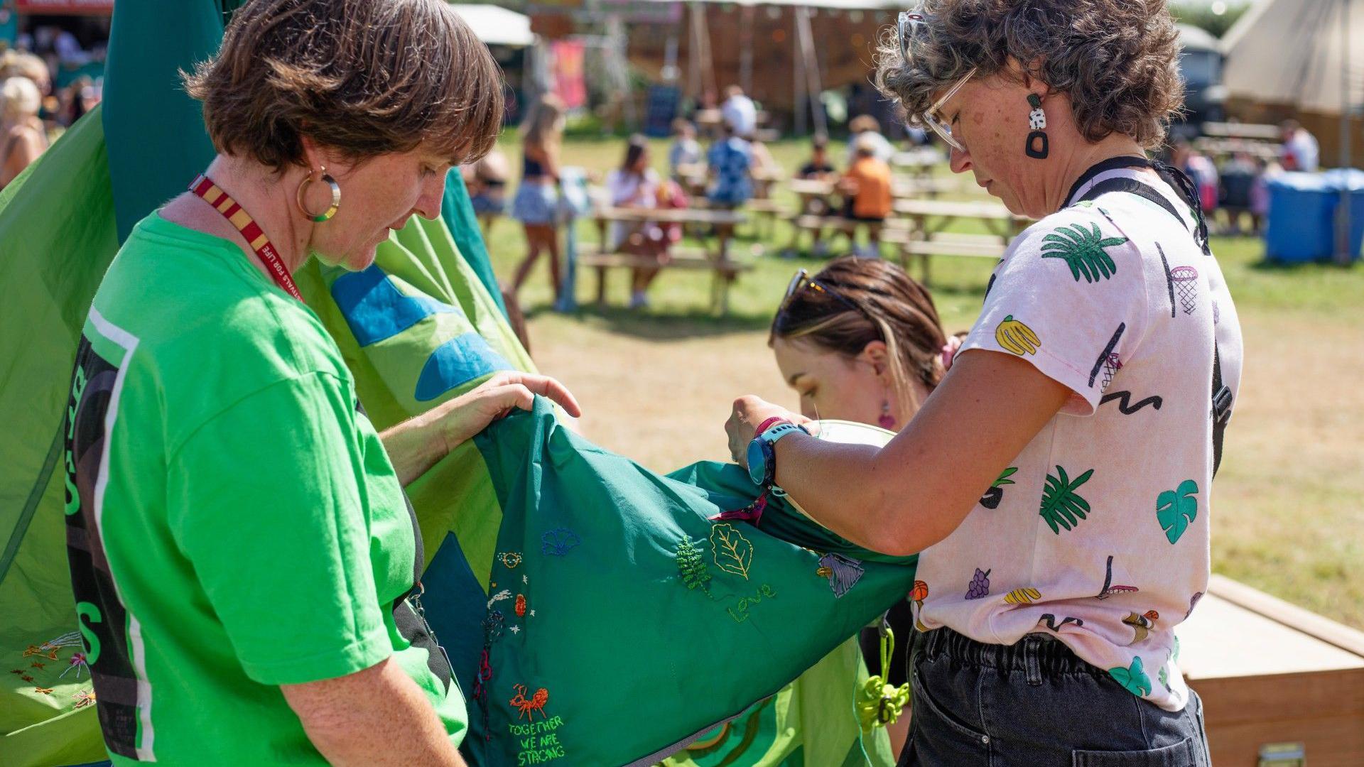 Two people sow messages into the Oxfam tent dress, which is on display at a festival.