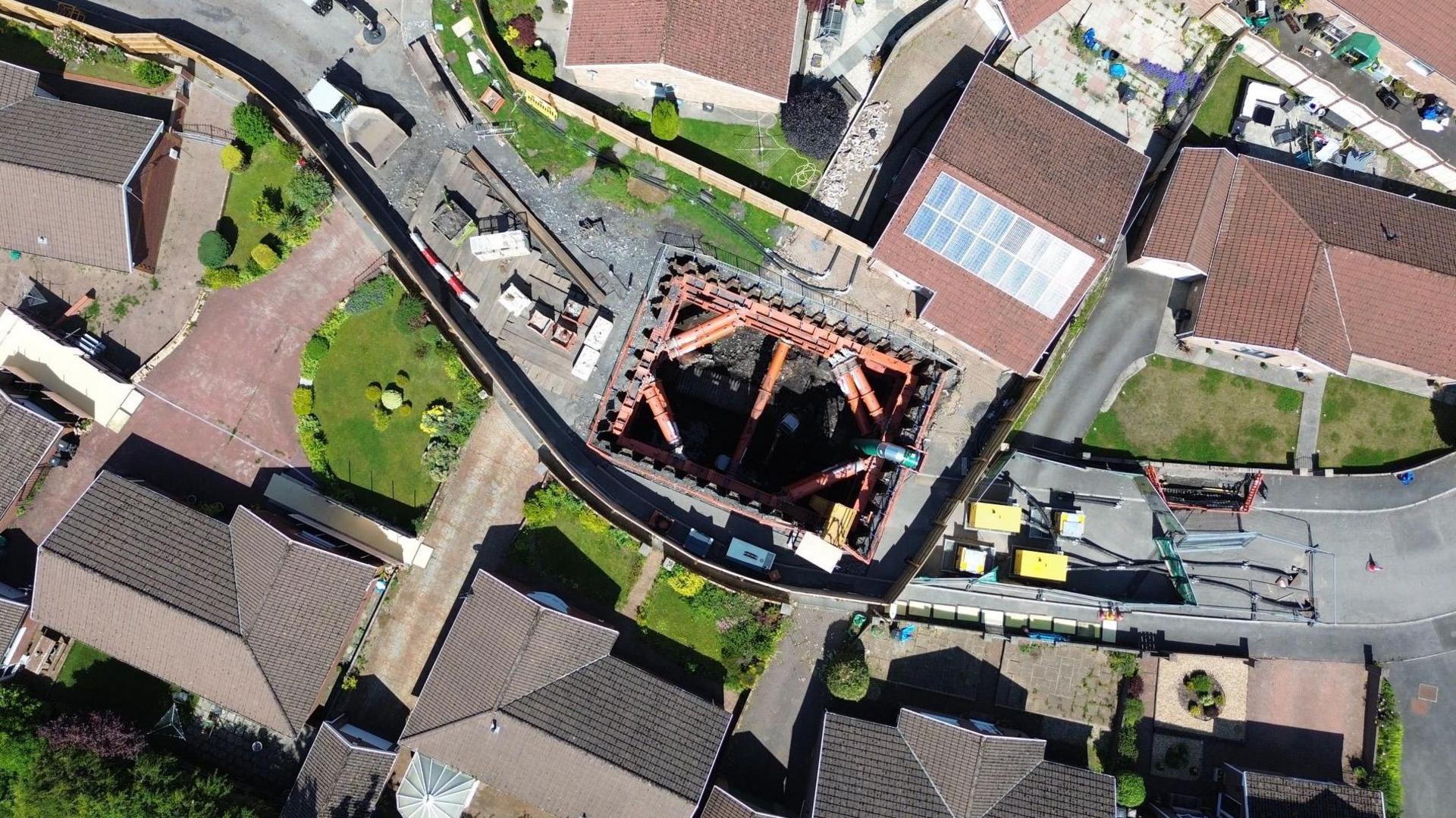 An aerial image of the 14 metre deep sinkhole with orange hydraulic bracing in place to secure the hole surrounded by houses on the estate. 