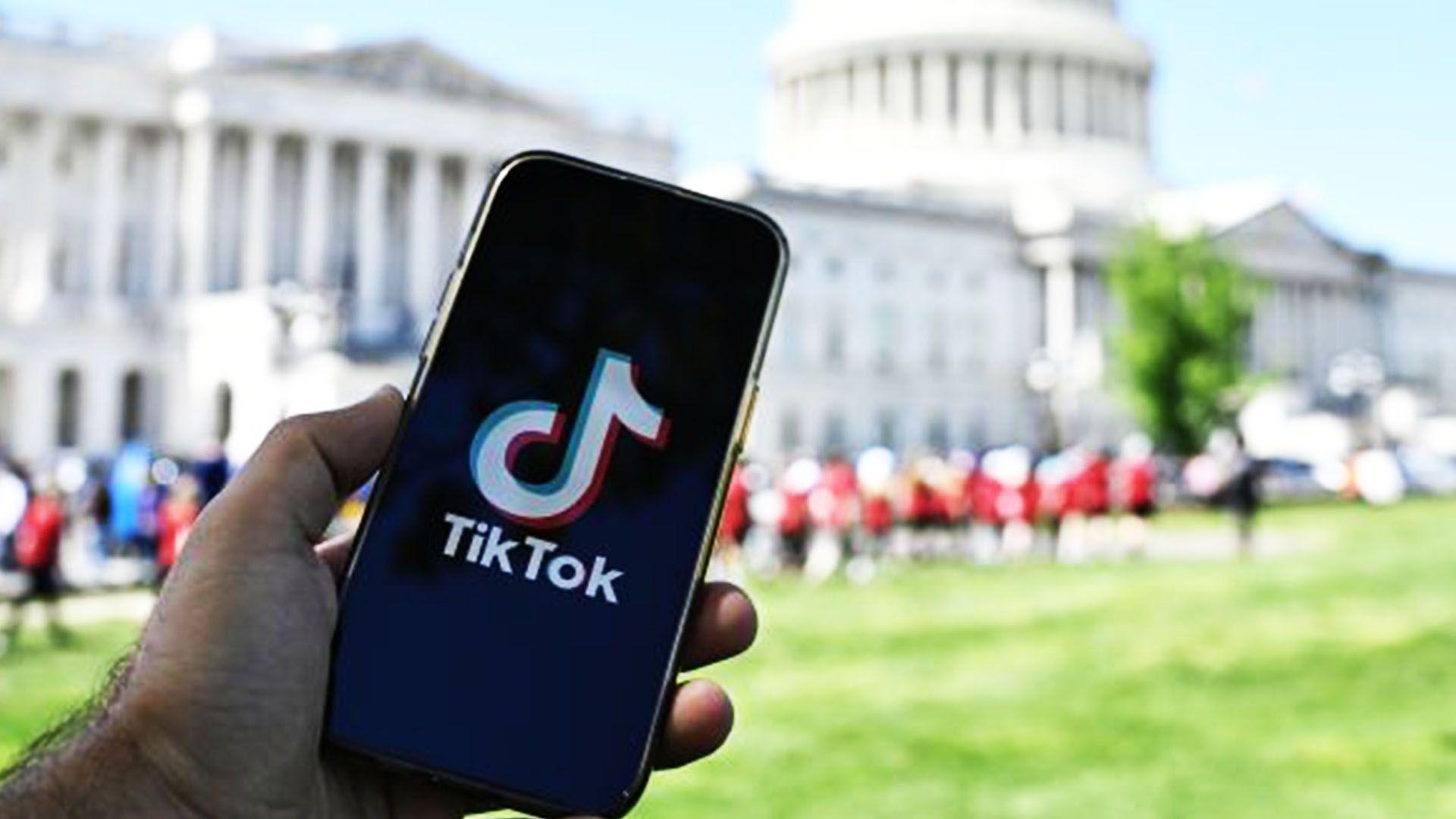 A hand holding a phone with the TikTok logo on it, int front of the US Capitol building