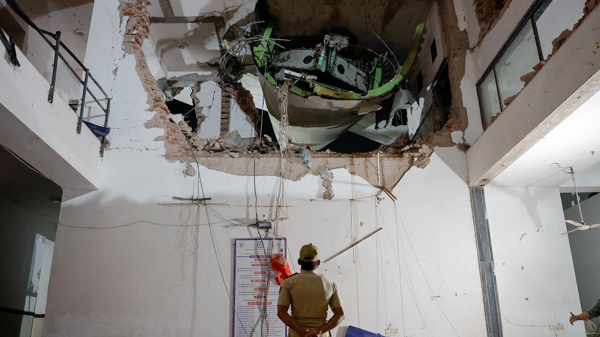 An official looks up with his arms behind his back and back turned to the camera, as they inspect a huge hole in the wall of a building interior, with some of the plane visible in the hole, on Thursday.