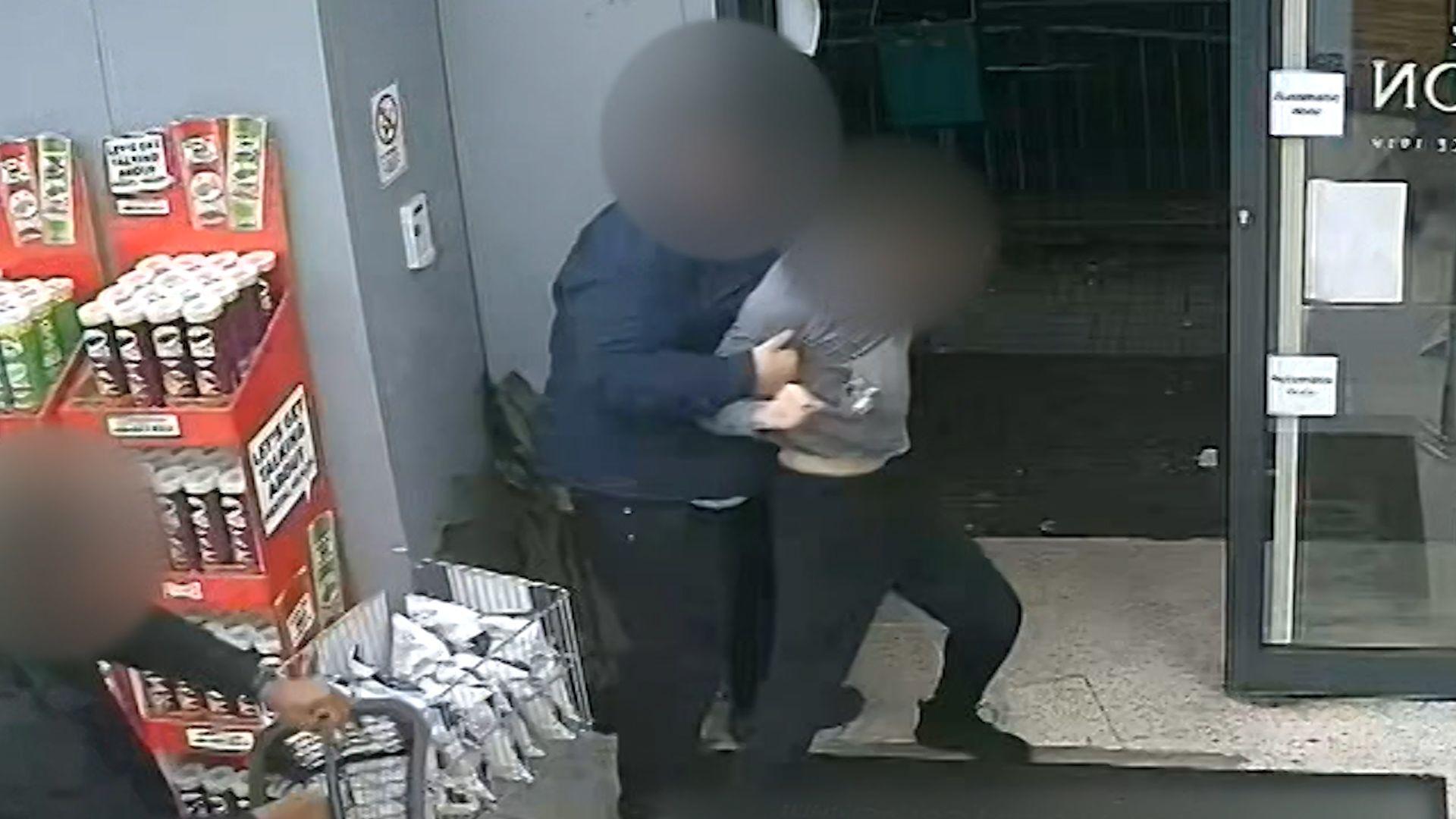 A man holding a shopping basket struggles with a shop worker near the exit of the store