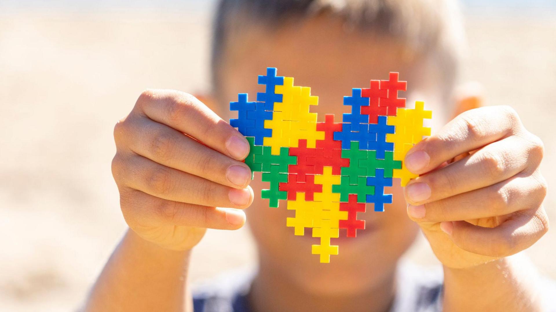 A boy holds up a colourful, heart-shaped puzzle in front of his face