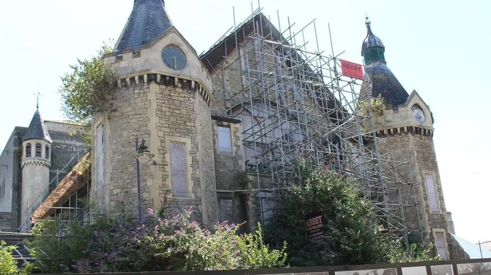 A Victorian building supported by scaffolding on the front. It has a pointed central roof with two turrets on each side of the main structure.