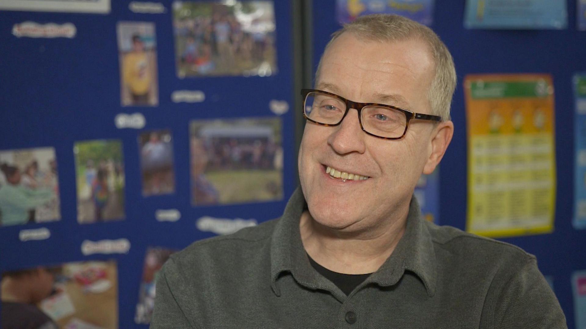 Paul Dobson smiles, wearing glasses and a grey polo shirt. He is sitting down, but only head and shoulders are visible.