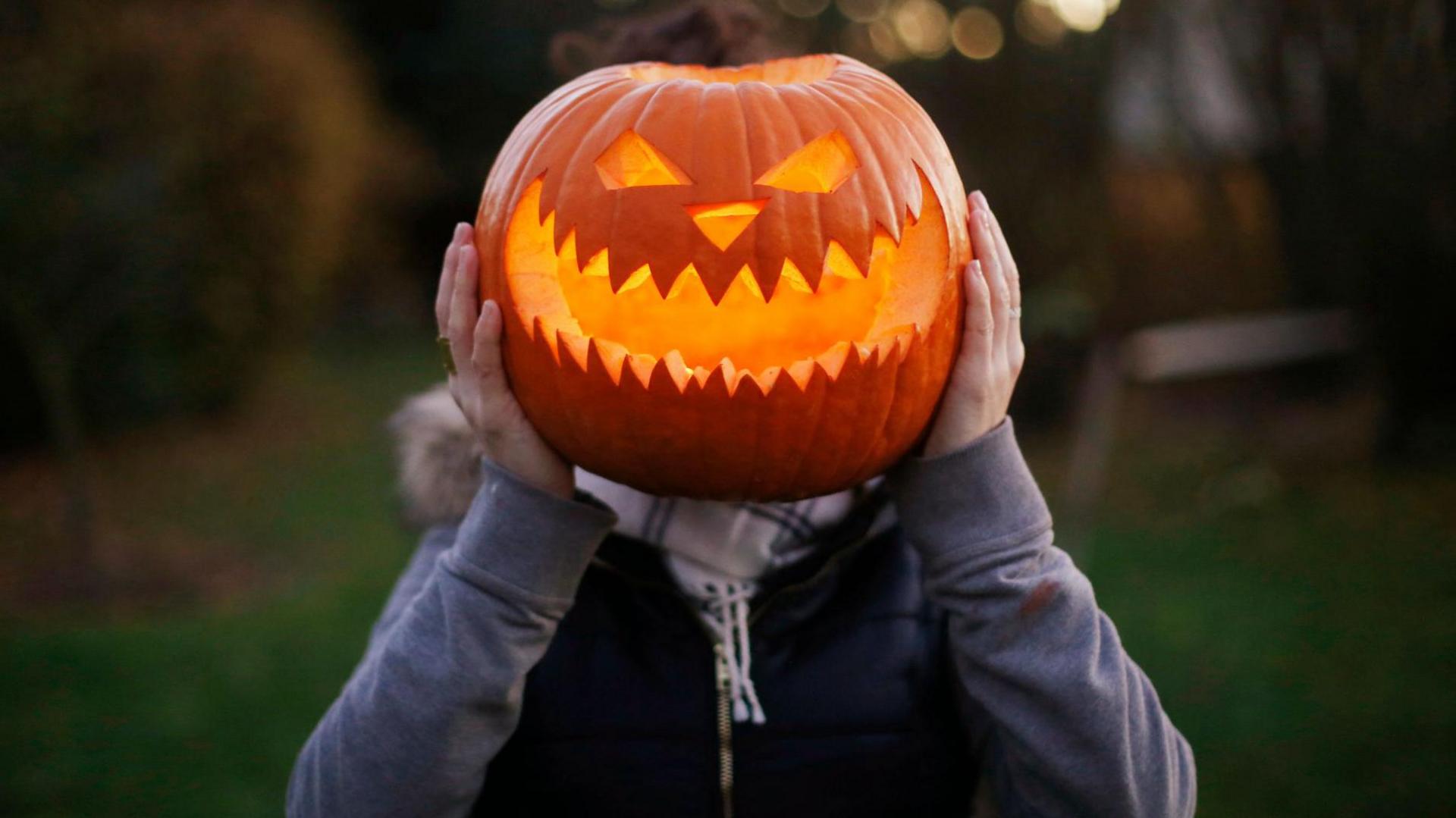 The image shows a person holding up a jack-o-lantern in front of their face