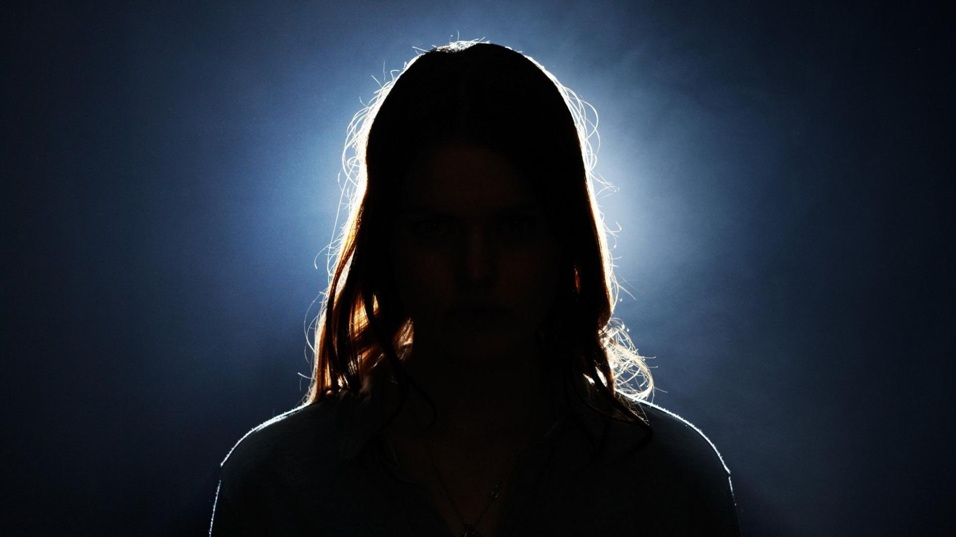 A young woman's head can be seen in silhouette, with a bright light and dark background behind her.