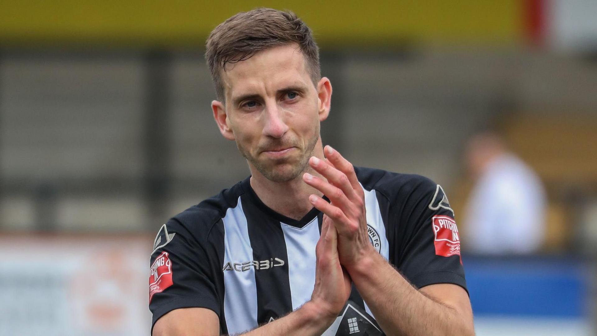 Wes Fogden clapping on the pitch in the black and white stripes of his Dorchester Town football kit.
