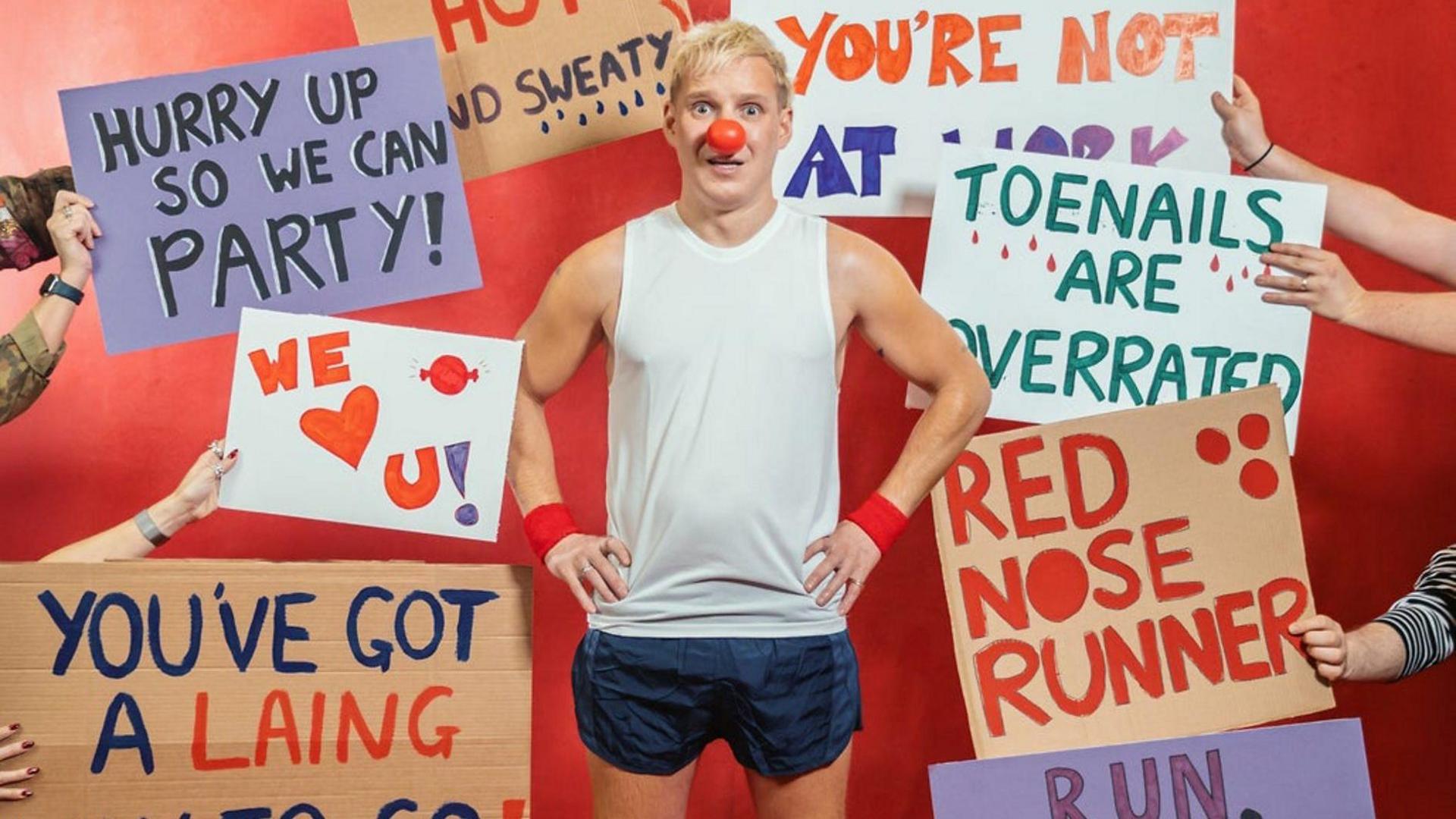 Jamie Laing in running clothes surrounded by signs supporting him.