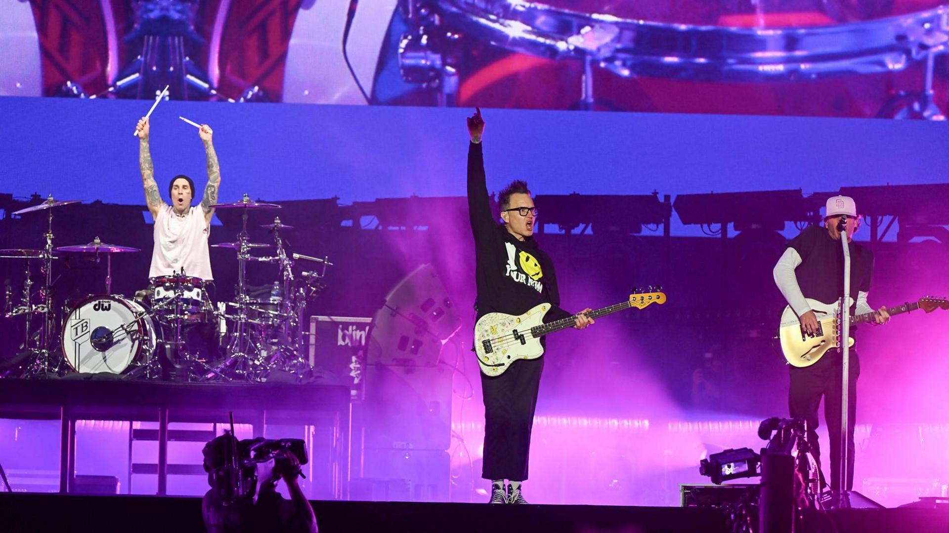 Blink-182 on stage with drummer Travis Barker holding his drumsticks aloft