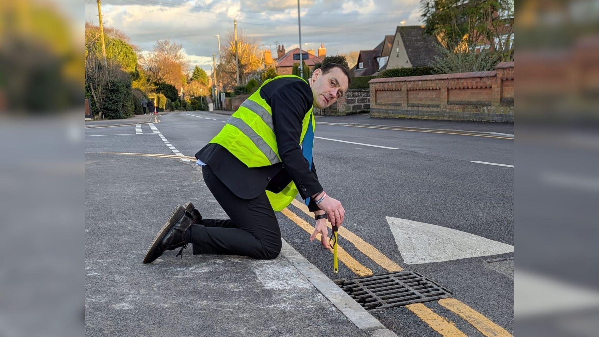 Ted Parton, in a hi vis jacket on Park Lane, measuring the height of the speed table at the edge of the road.