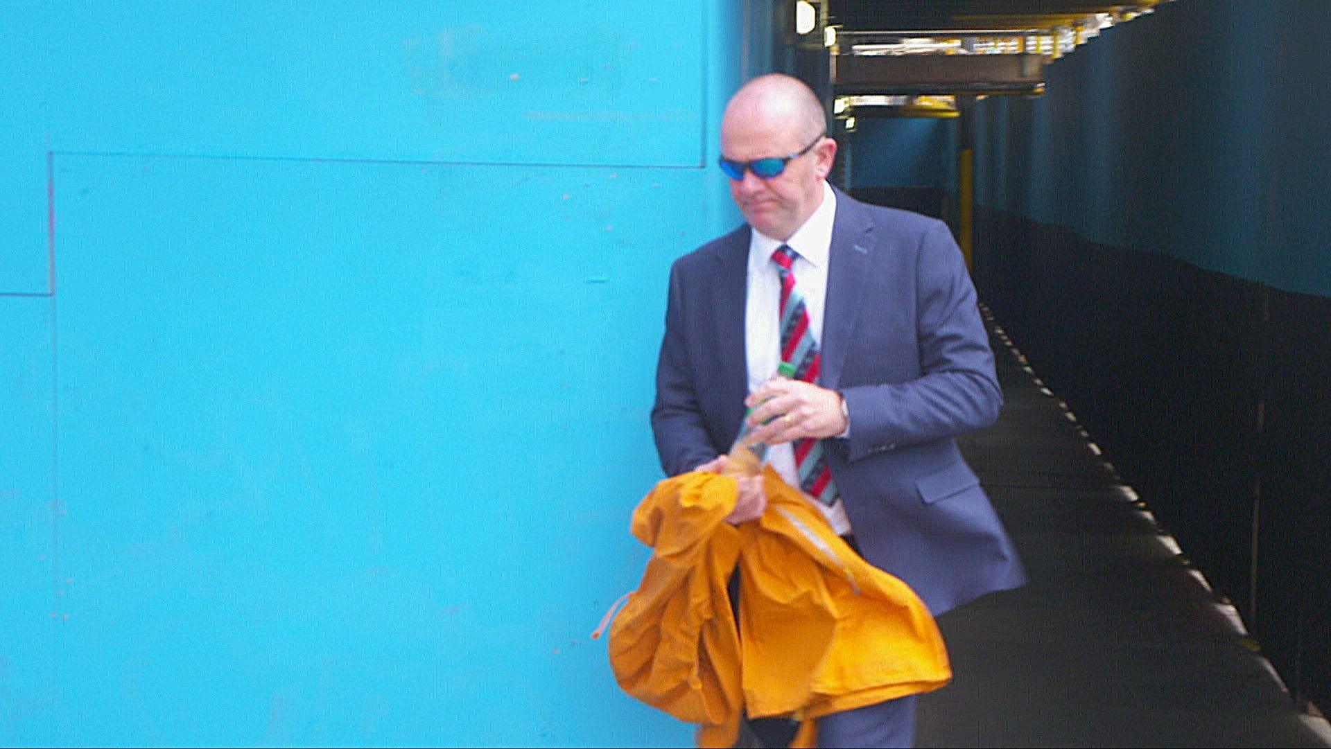 Keith Warhurst in blue suit and white shirt with striped tie leaving court. He is wearing dark glasses and is bald.