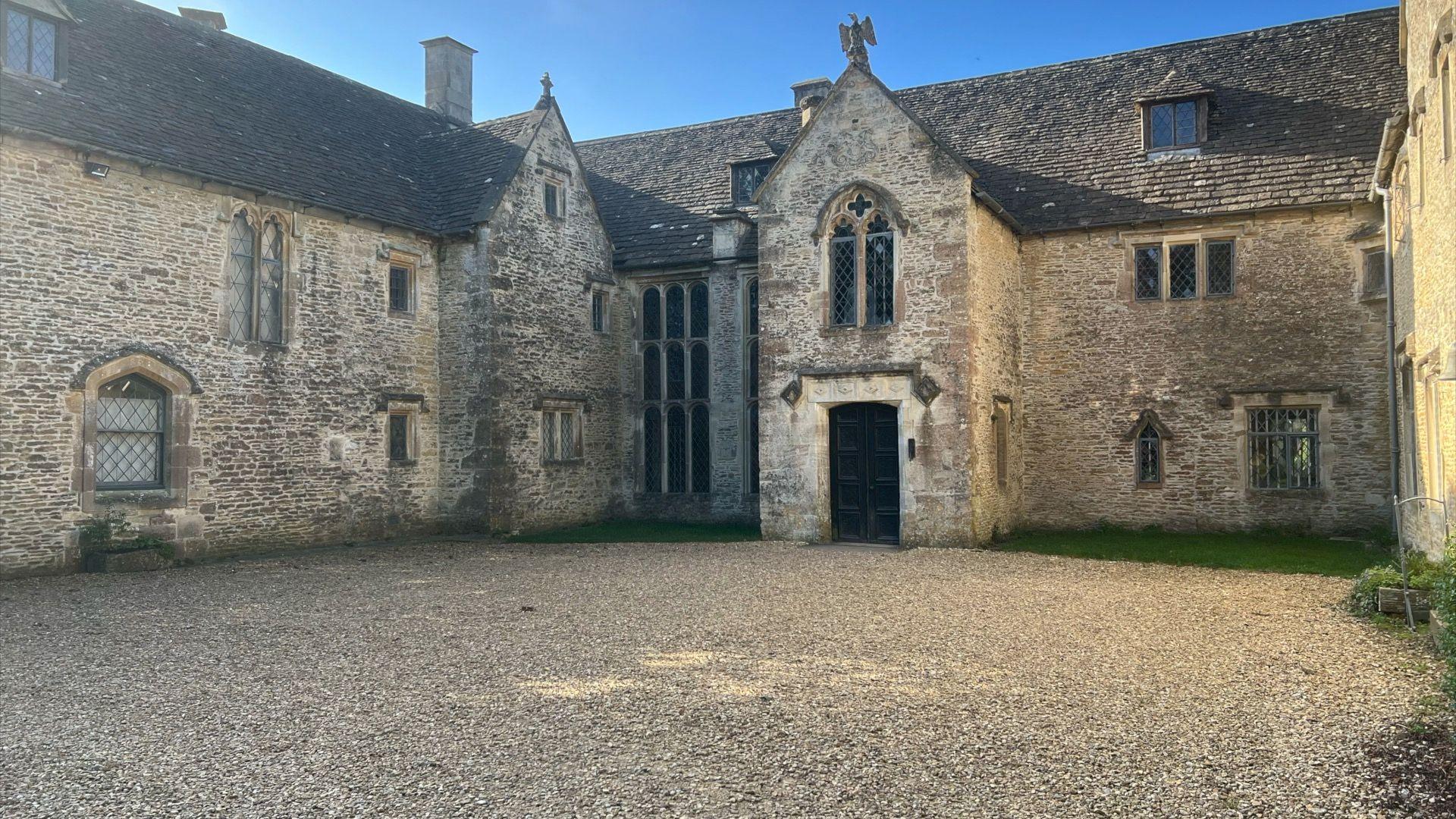 Large cotswold brick house with huge stone driveway and rustic looking windows.