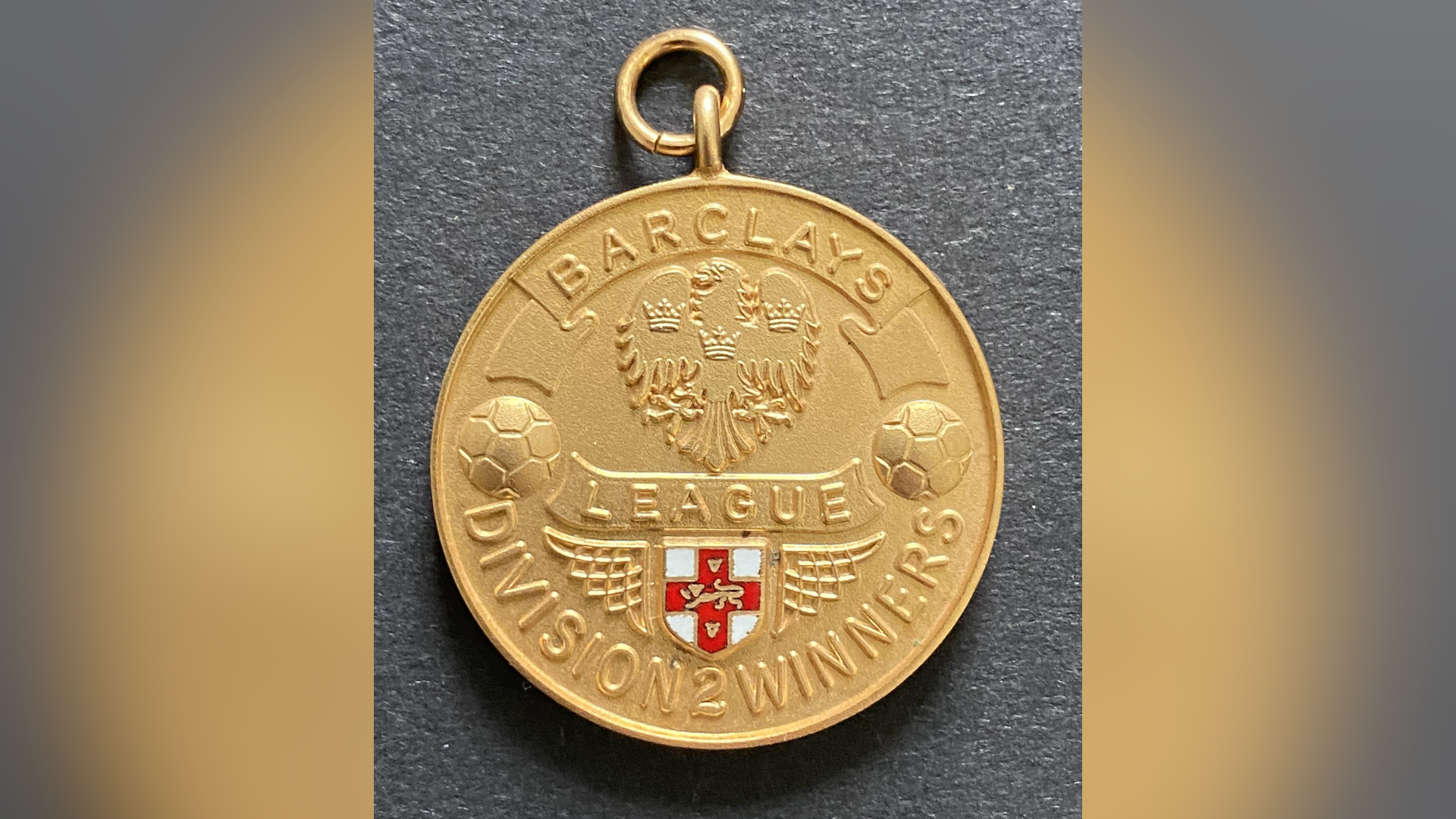 A gold medal that reads Barclays League Division 2 Winners on it rests on a grey surface.