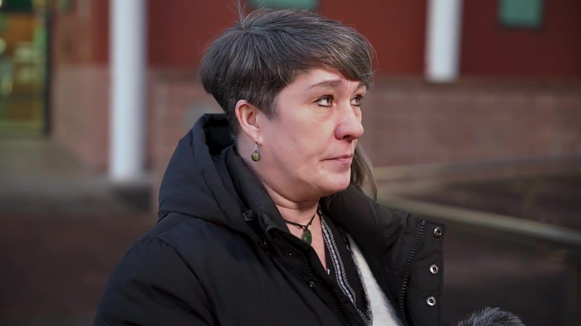 Marie, who has short dark brown hair and wears a black coat, speaks to the camera outside Preston Crown Court with a serious expression on her face.