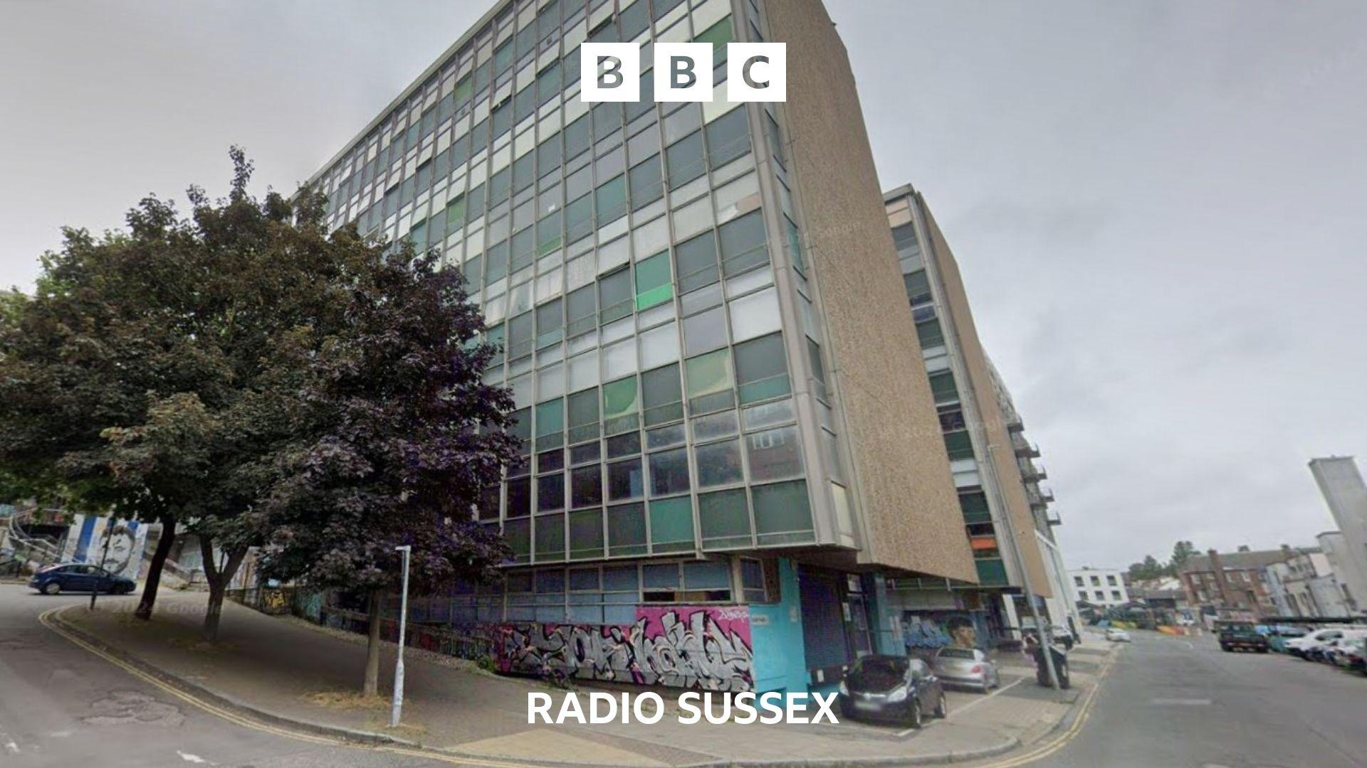 Exterior shot of a 1960's tower block. There is a tree on the left and graffiti at the base of the building.