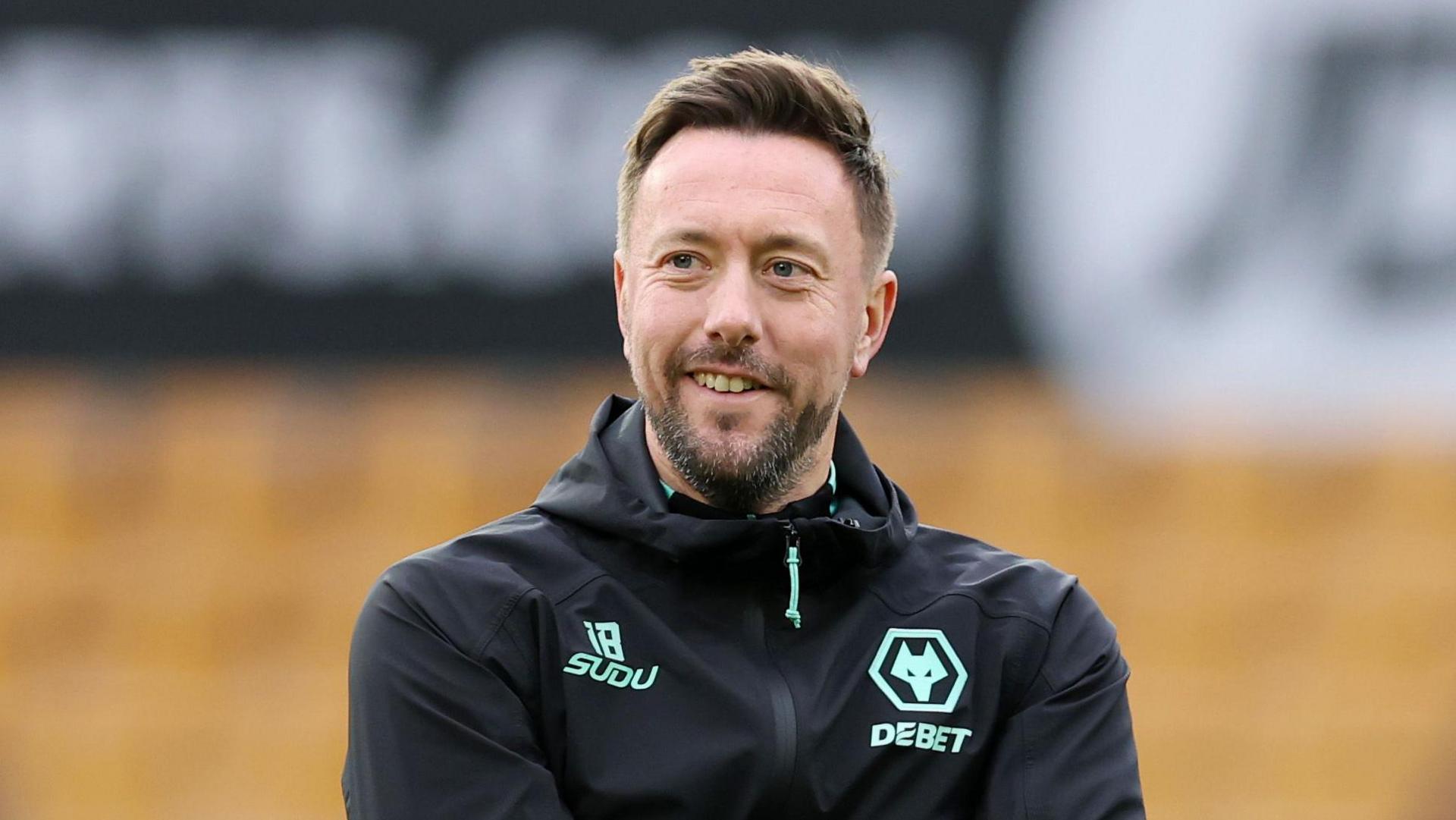 Ian Burchnall wearing a jacket with Wolves logo while looking on at a training session