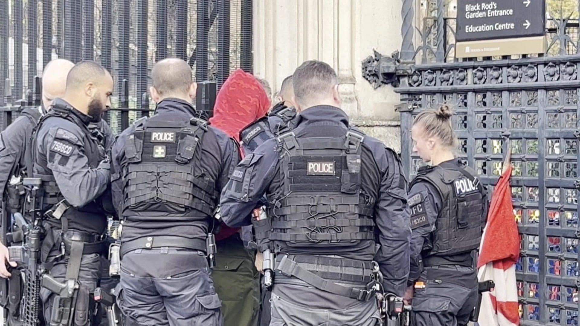 Police officers arrest a man in a red hoodie.