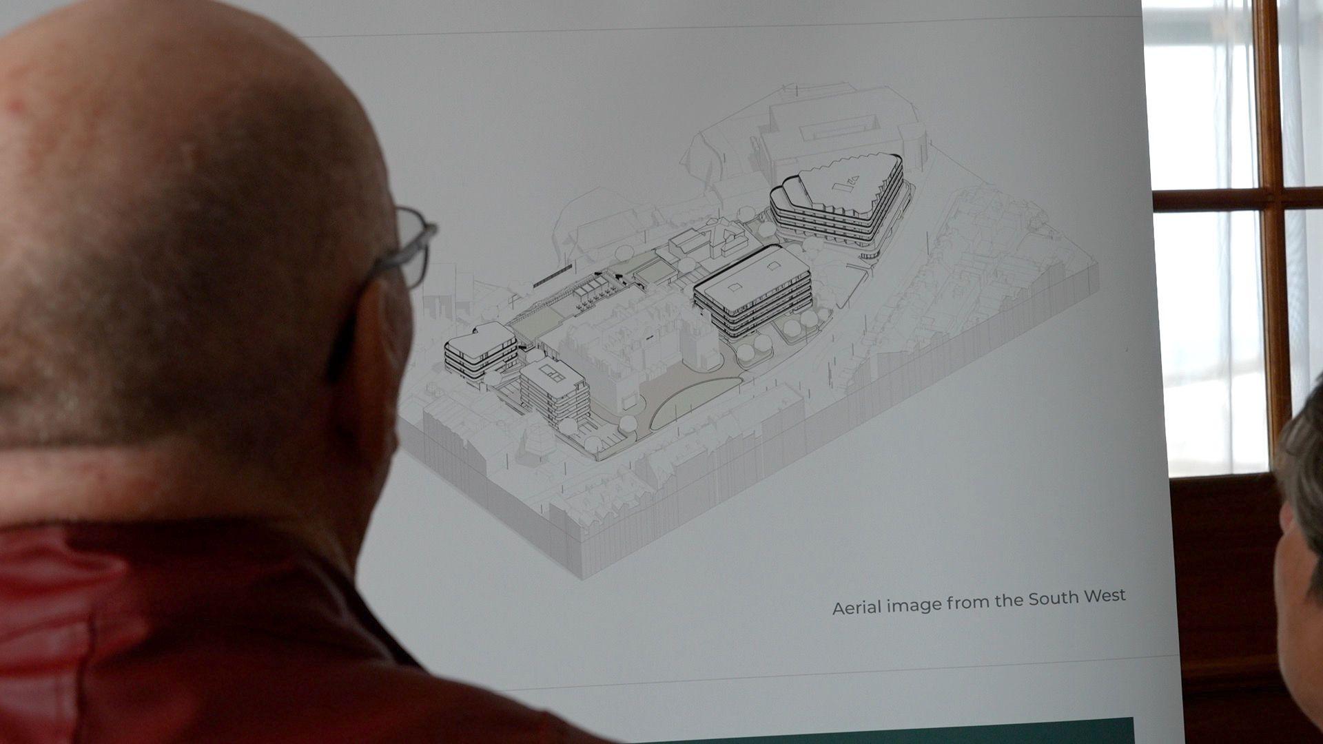 A bald man looking away at at computer generated plan of what the site could look like