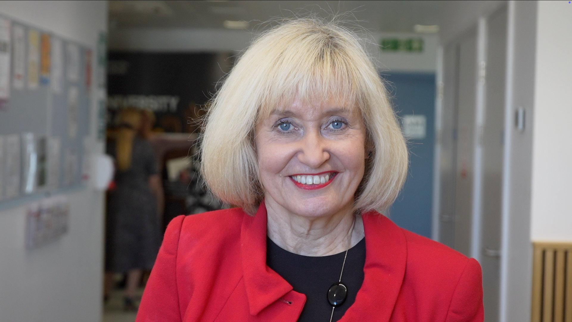 Professor Jenny Higham smiles at the camera. She has short blonde hair and wears a red blazer with a black top underneath.