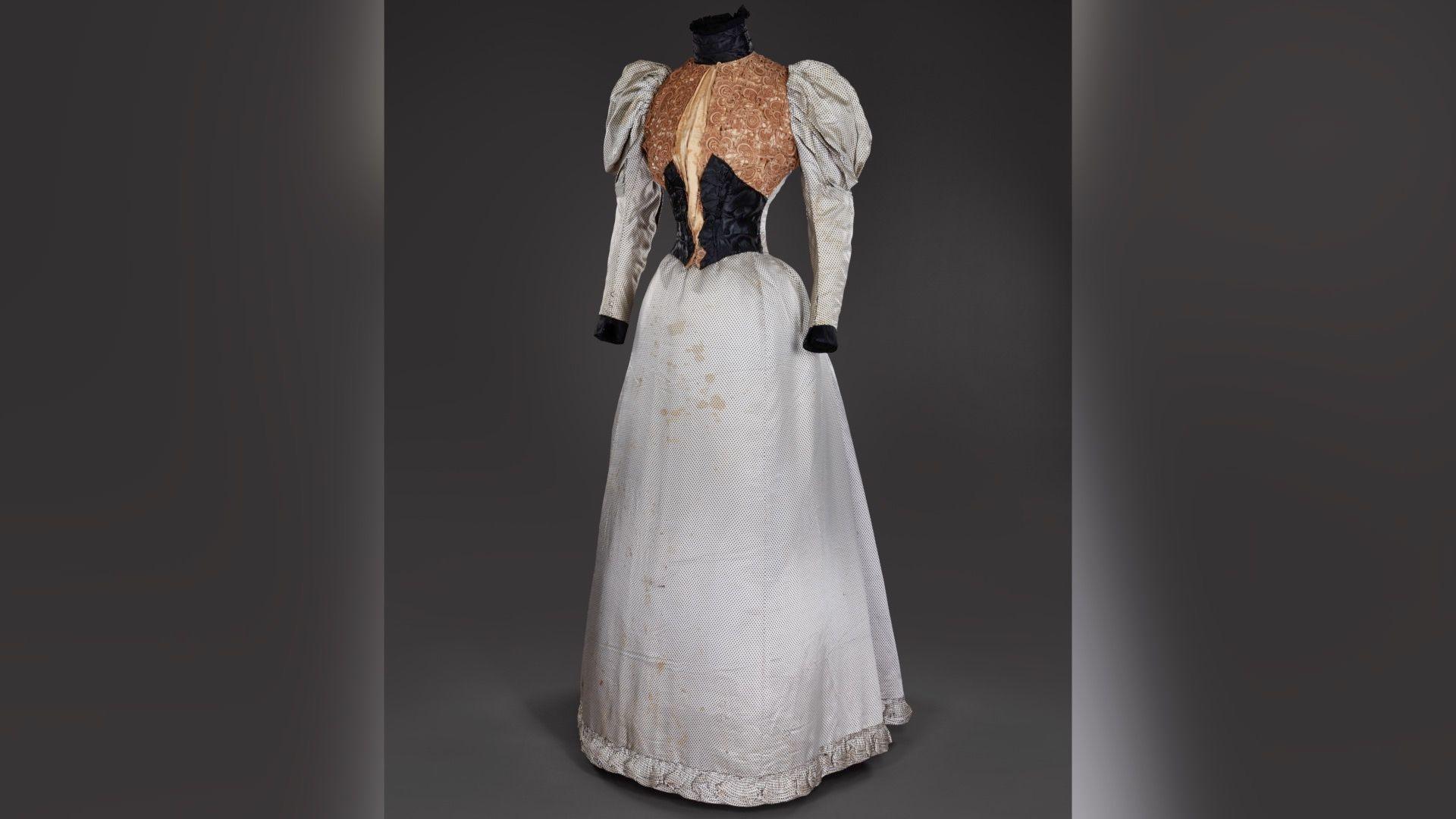 A slightly dirty, silver dress with puffy sleeves, the waist is black and the chest area is covered in gold detail. 