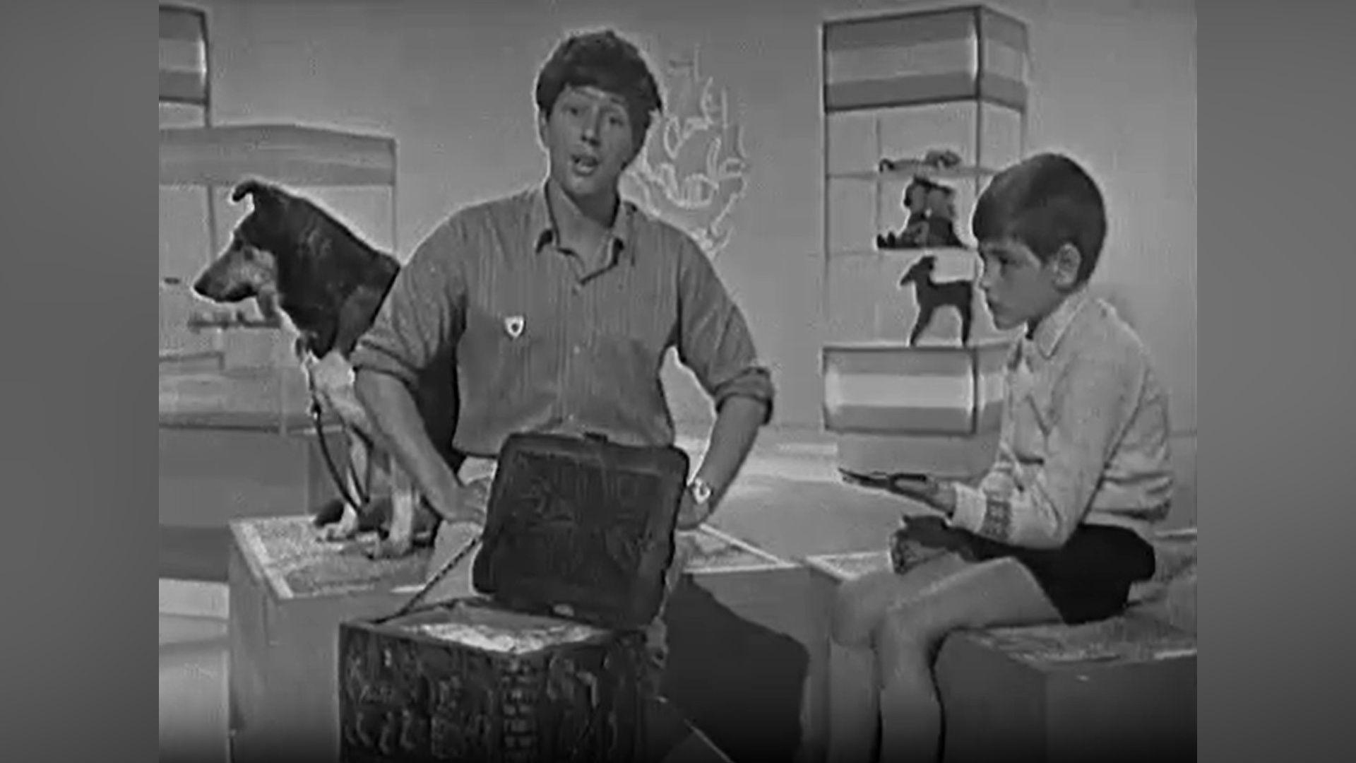 Pamje bardhë e zi nga një edicion i shtatorit 1968 i Blue Peter, me prezantuesin John Noakes në studio me David Welham, i cili mban monedhat e tij.