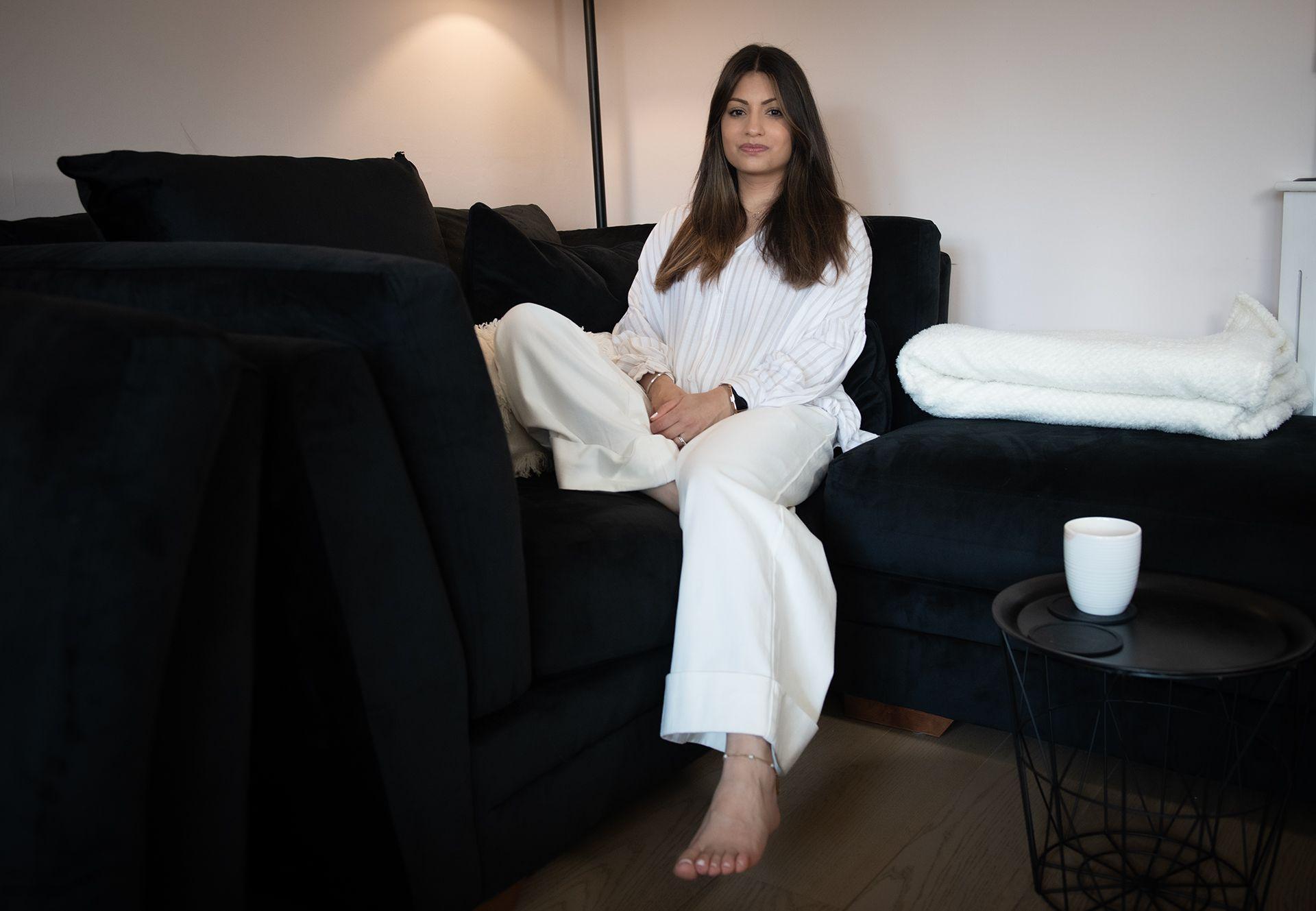 Jasleen is wearing all white sat on a sofa with a cup of tea next to her