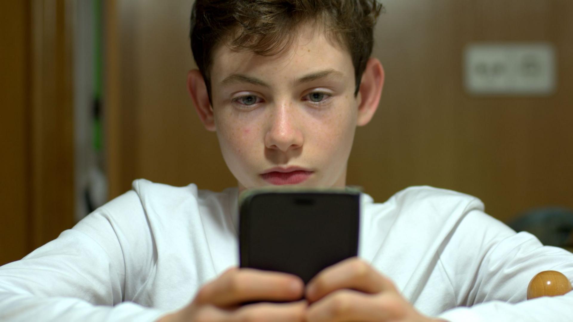 A stock image showing a teenage boy using a smartphone