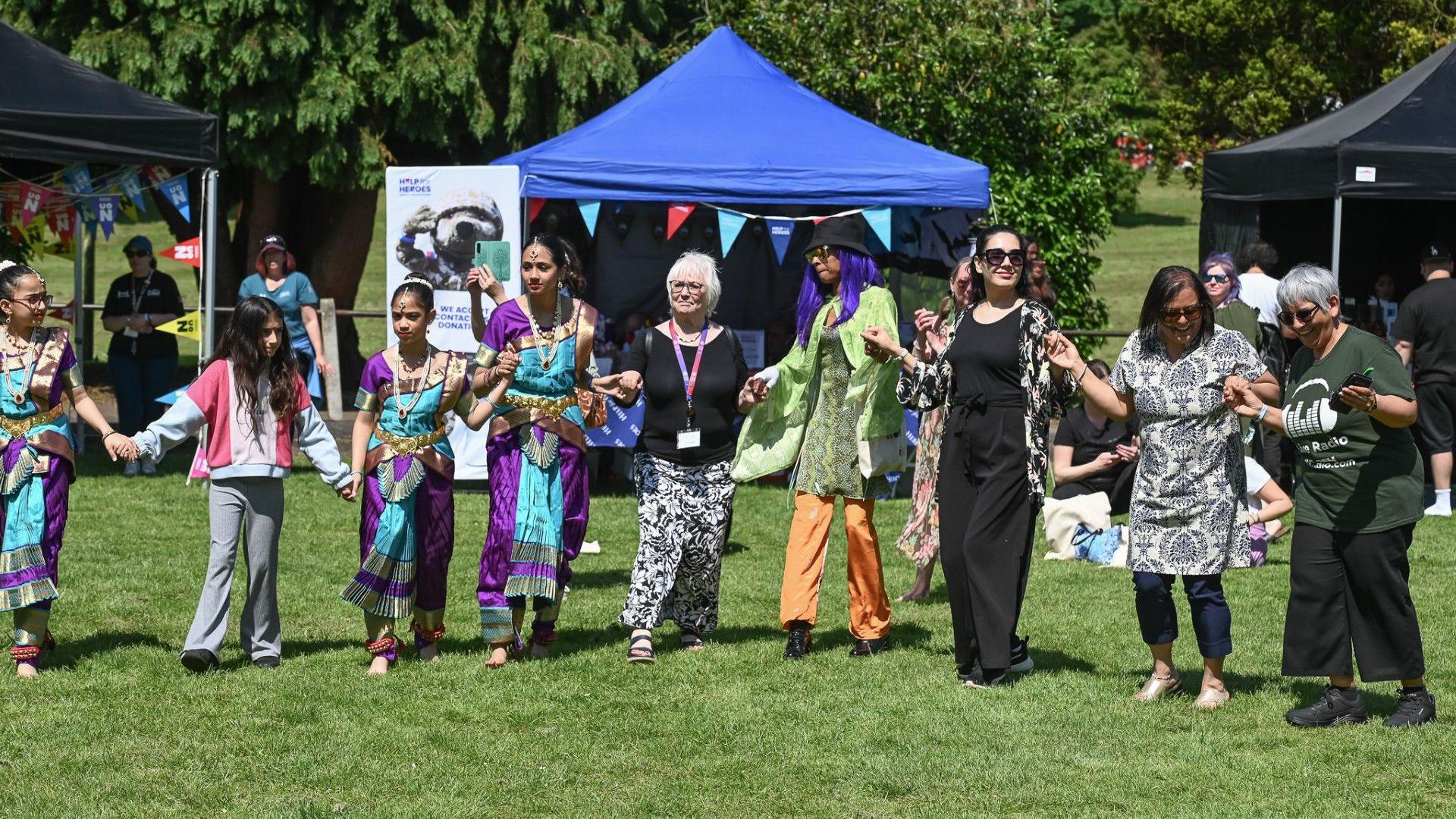 Eid celebrations taking place at Northampton’s Becket’s Park. People are holding hand and standing in a line while standing on the grass.