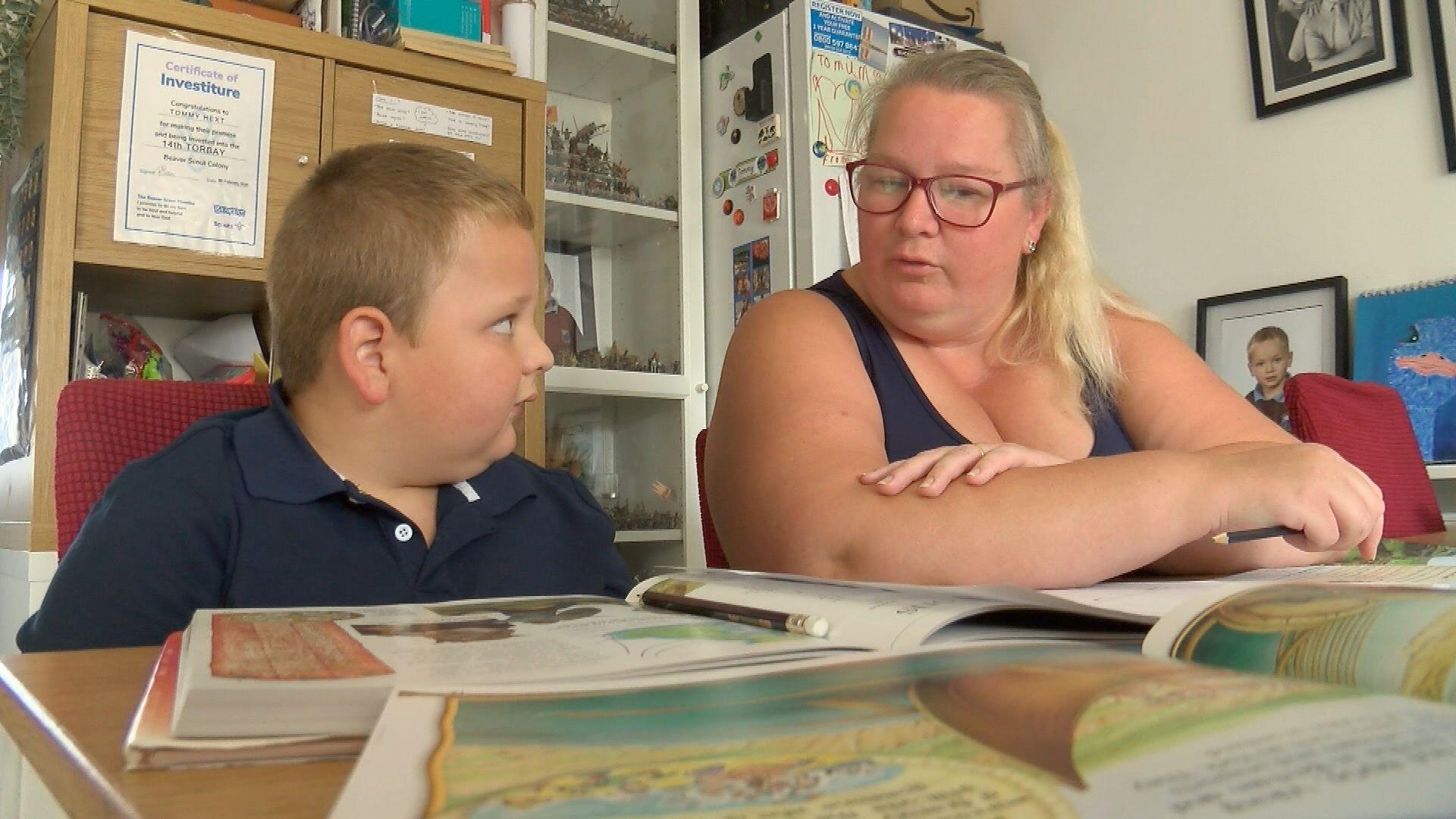 Tommy, 7, sitting at a table with books being home educated by his mother Rachel