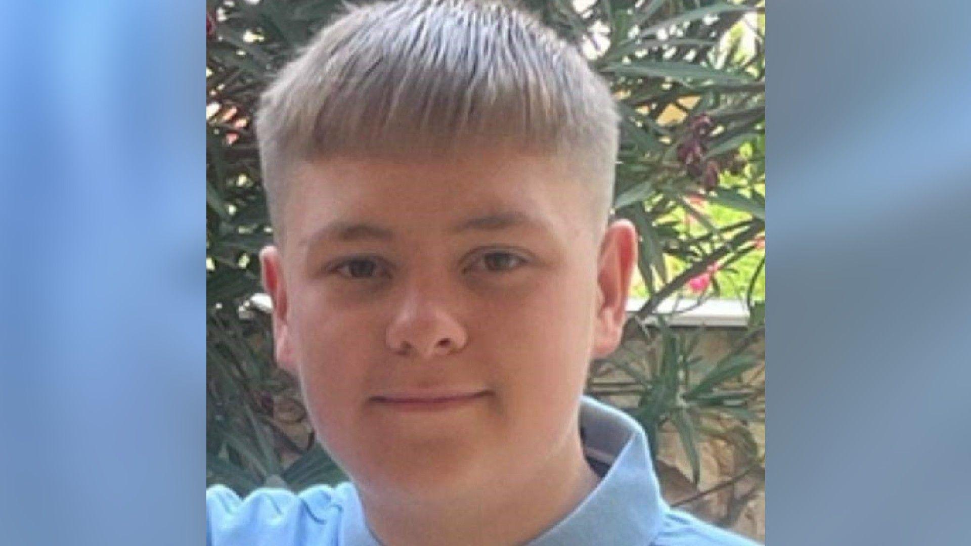 A photo of Harvey when he was slightly younger - maybe about 13. He has the same haircut, straight across his forehead and short at the sides, as in more recent photos. He wears a light blue shirt with a collar. He is smiling slightly at the camera and appears to be in a garden, possibly on holiday.