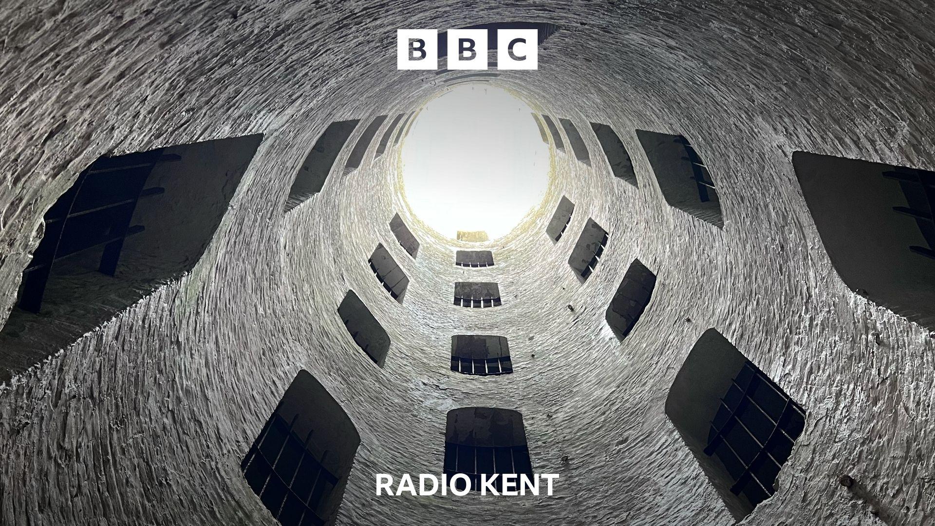 The inside of a tall brick tower reaches into the sky. Dotted around the tower are openings with metal railings.