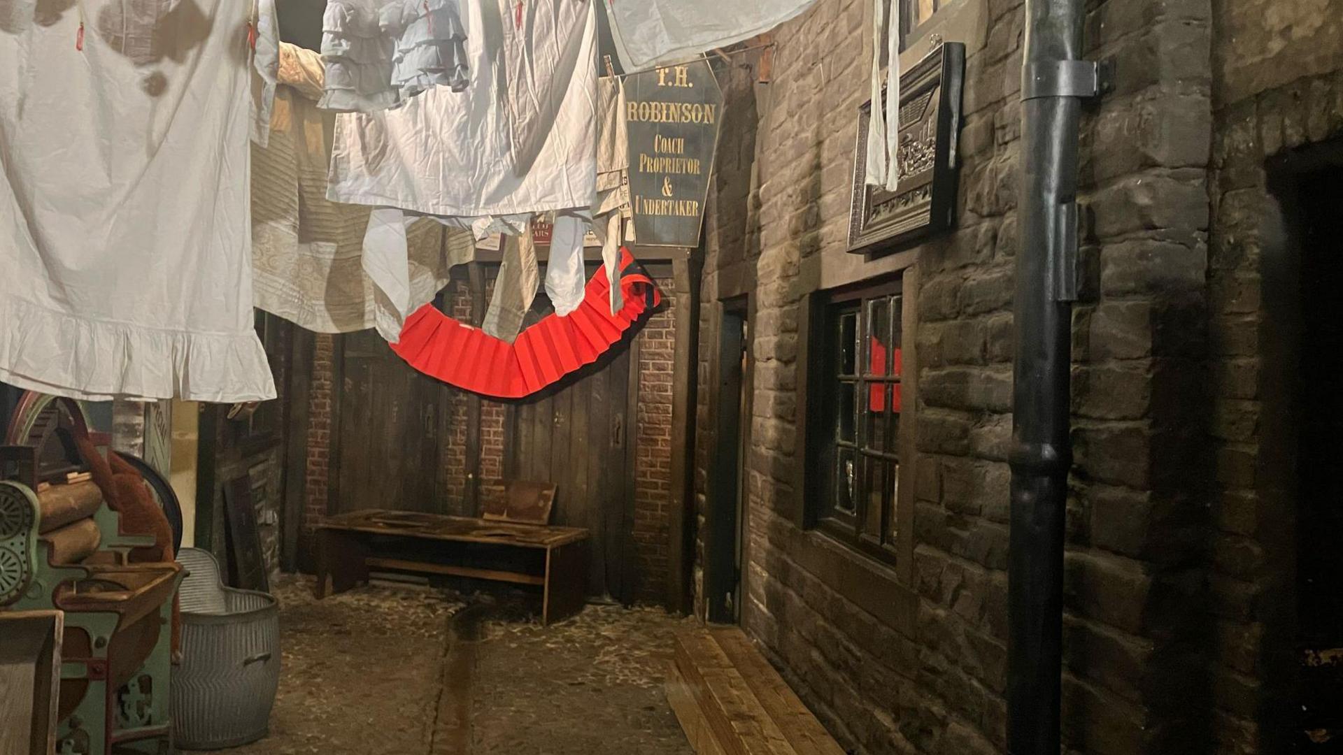 Cobbled streets are lined by a York stone terraced row. Laundry loads are strung up above the streets.