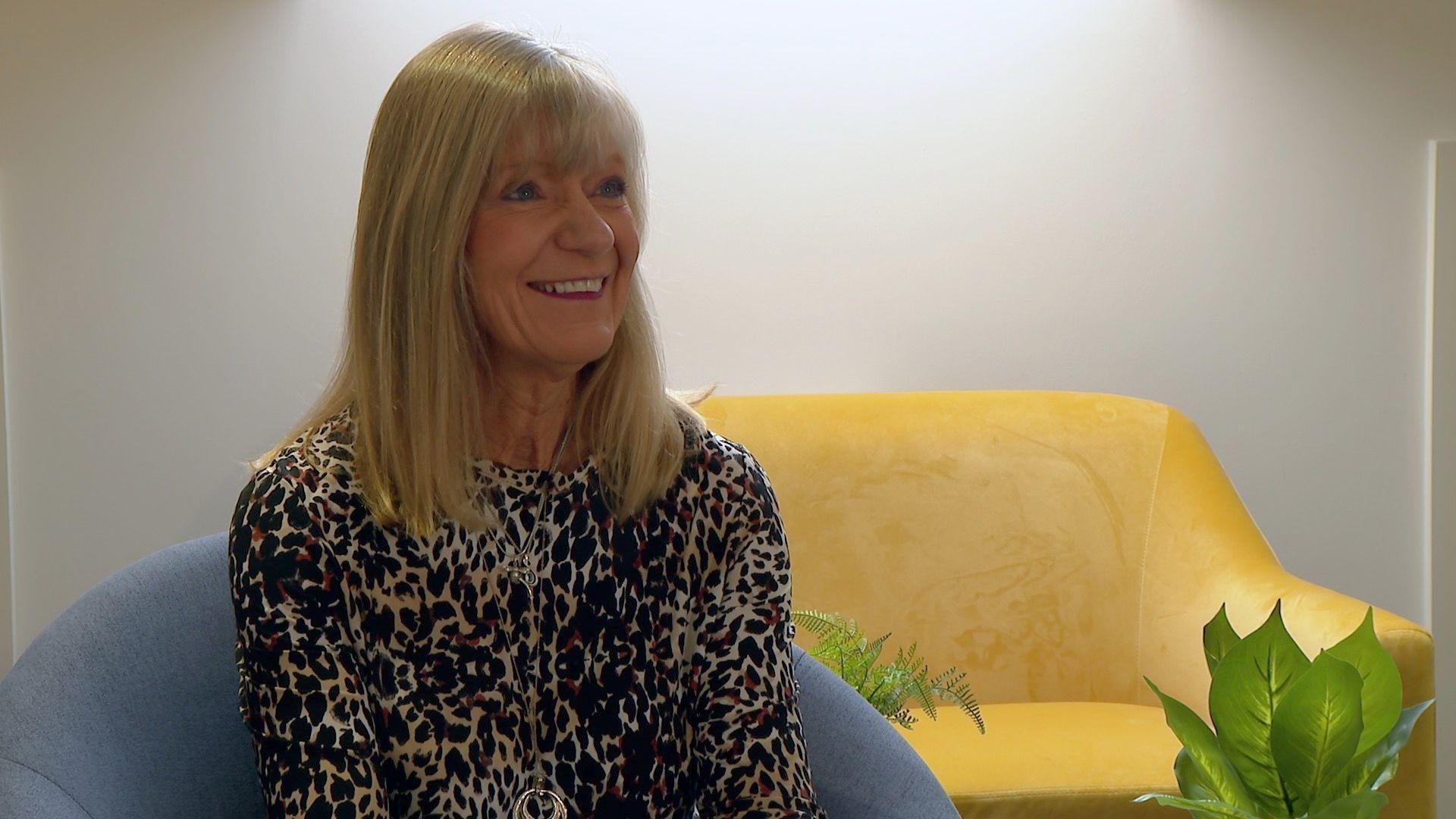 A woman with long blonde hair sits on a blue chair