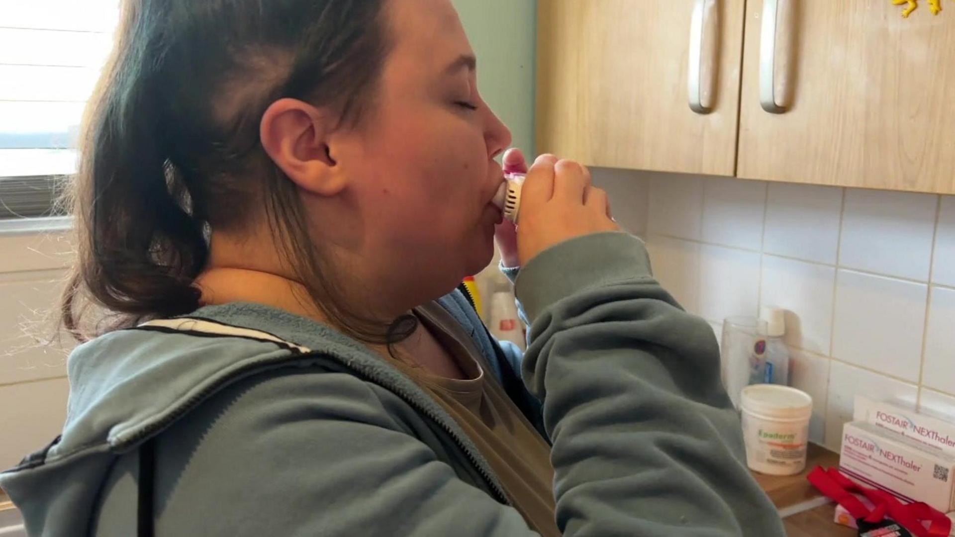 Lou in her kitchen using an inhaler