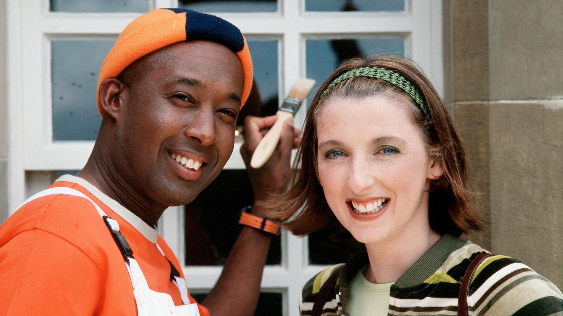 Rodd Christensen, as Spencer the Painter, and Julie Wilson Nimmo, as Miss Hoolie the nursery teacher, stand in front of a window frame Spencer is painting