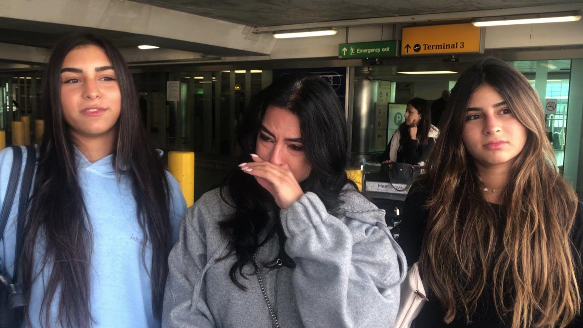 Nadine, a UK national, is visibly upset as she stands with her two daughters, Lea, 17 (standing on the left-hand side) and Yasmina, 15 (on the right-hand side) at Heathrow airport. Behind them there is a sign pointing towards Terminal 3.