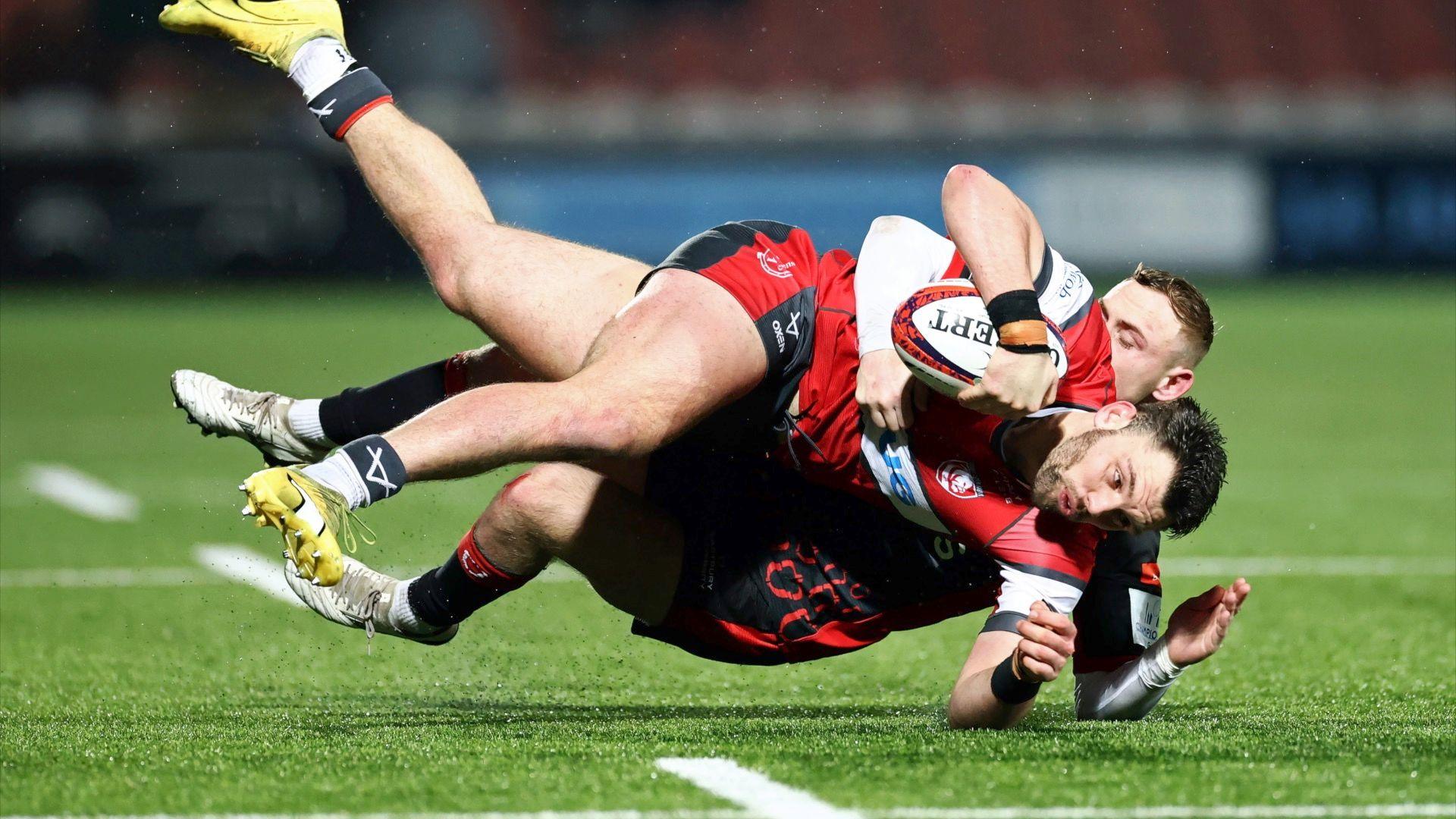 Two rugby players tackling each other to the ground with a rugby ball in hand.