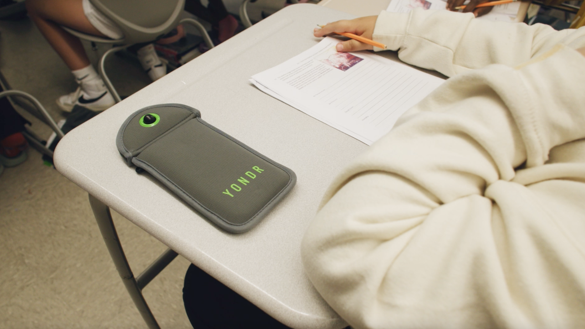 A Yondr pouch on the desk as a child sits a test.