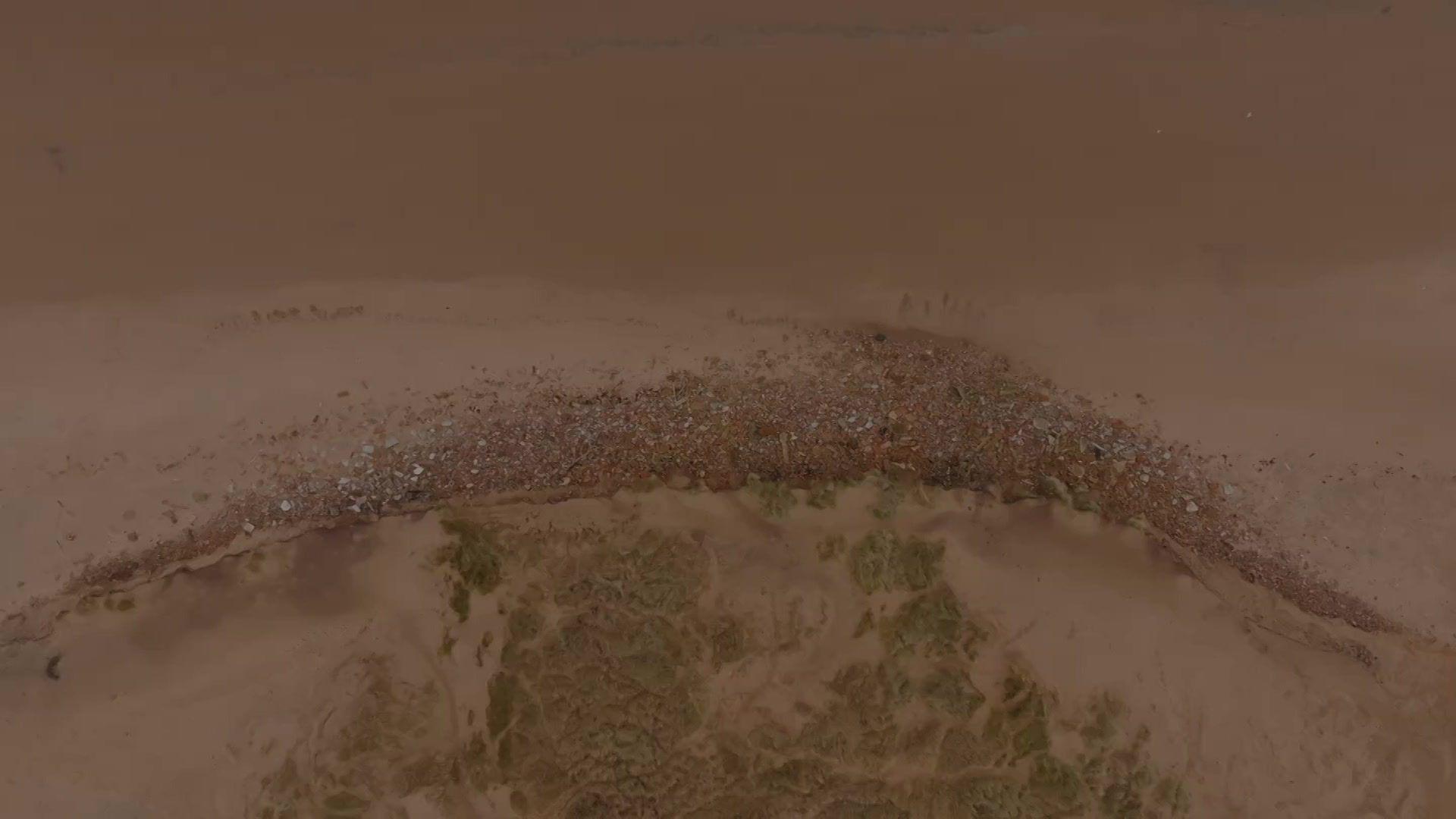 An aerial picture of a stretch of beach with rubble curving around a sand dune 