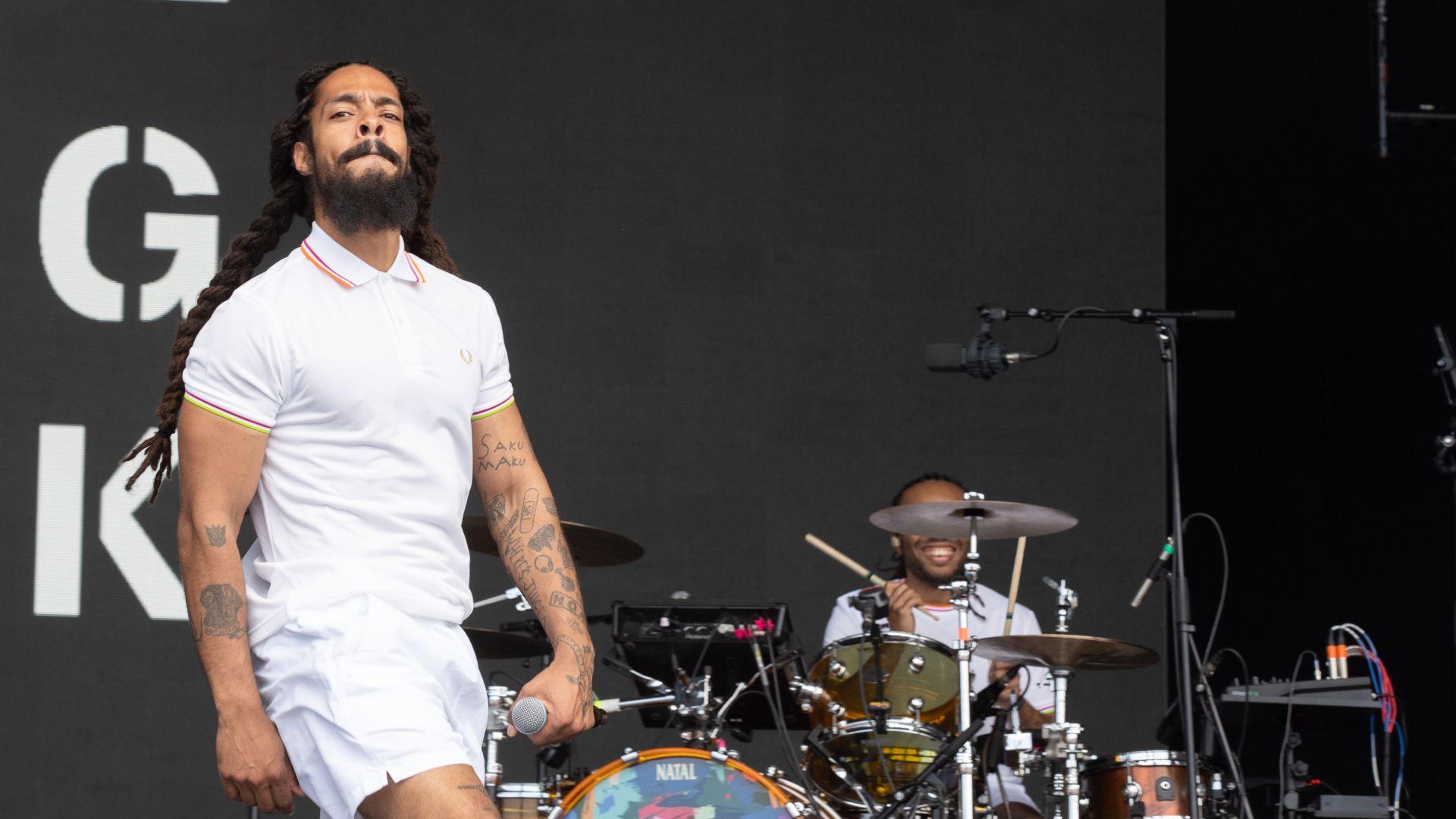 Bobby Vylan, a man with long brown hair and dressed in a white polo t-shirt and shorts, performs on stage at Glastonbury.