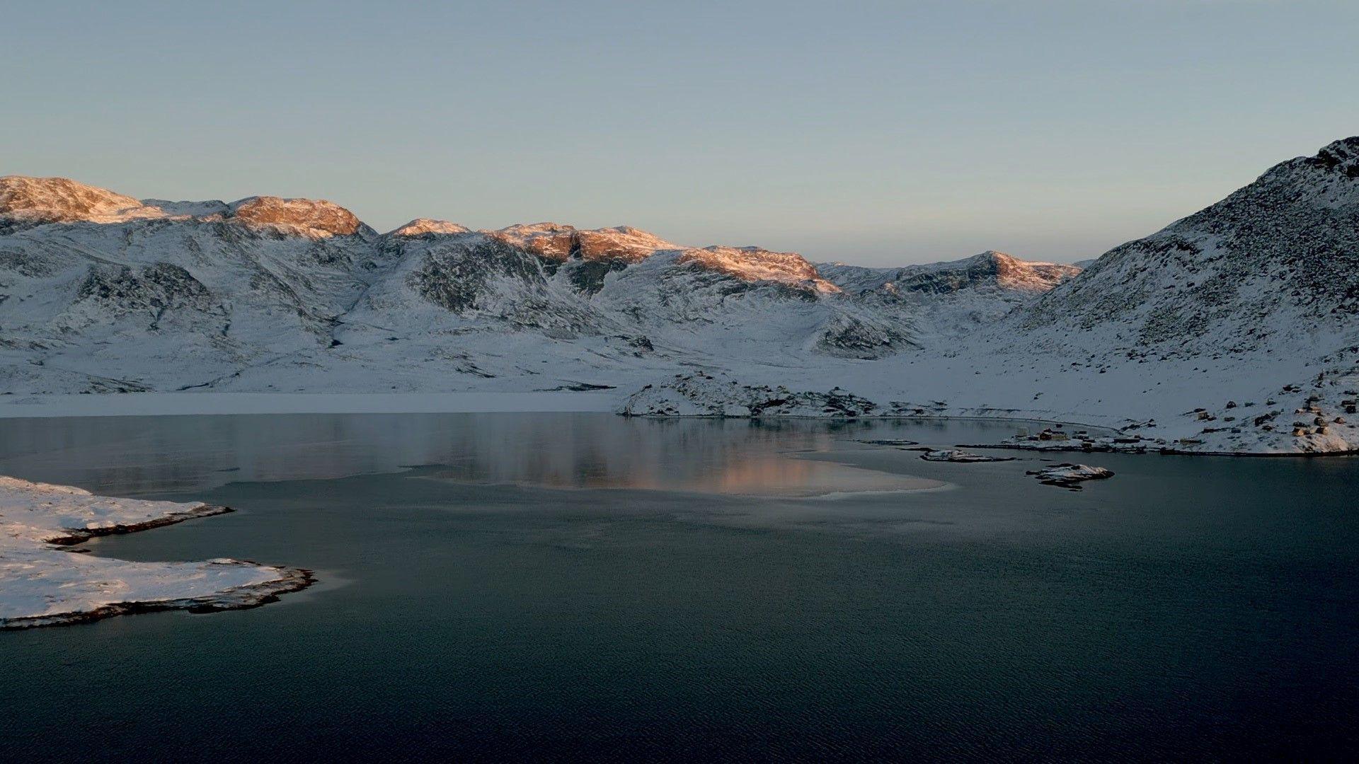 A drone image of a fjord with snow covered mountains in the background