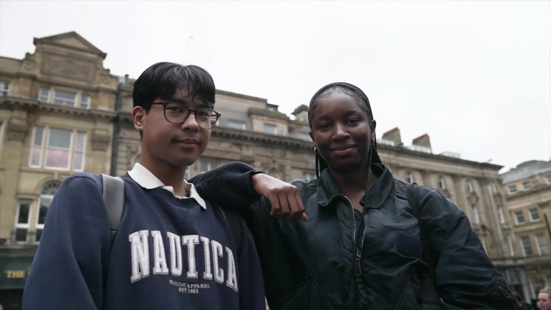 Two young people standing side by side, with a grand ancient building behind them