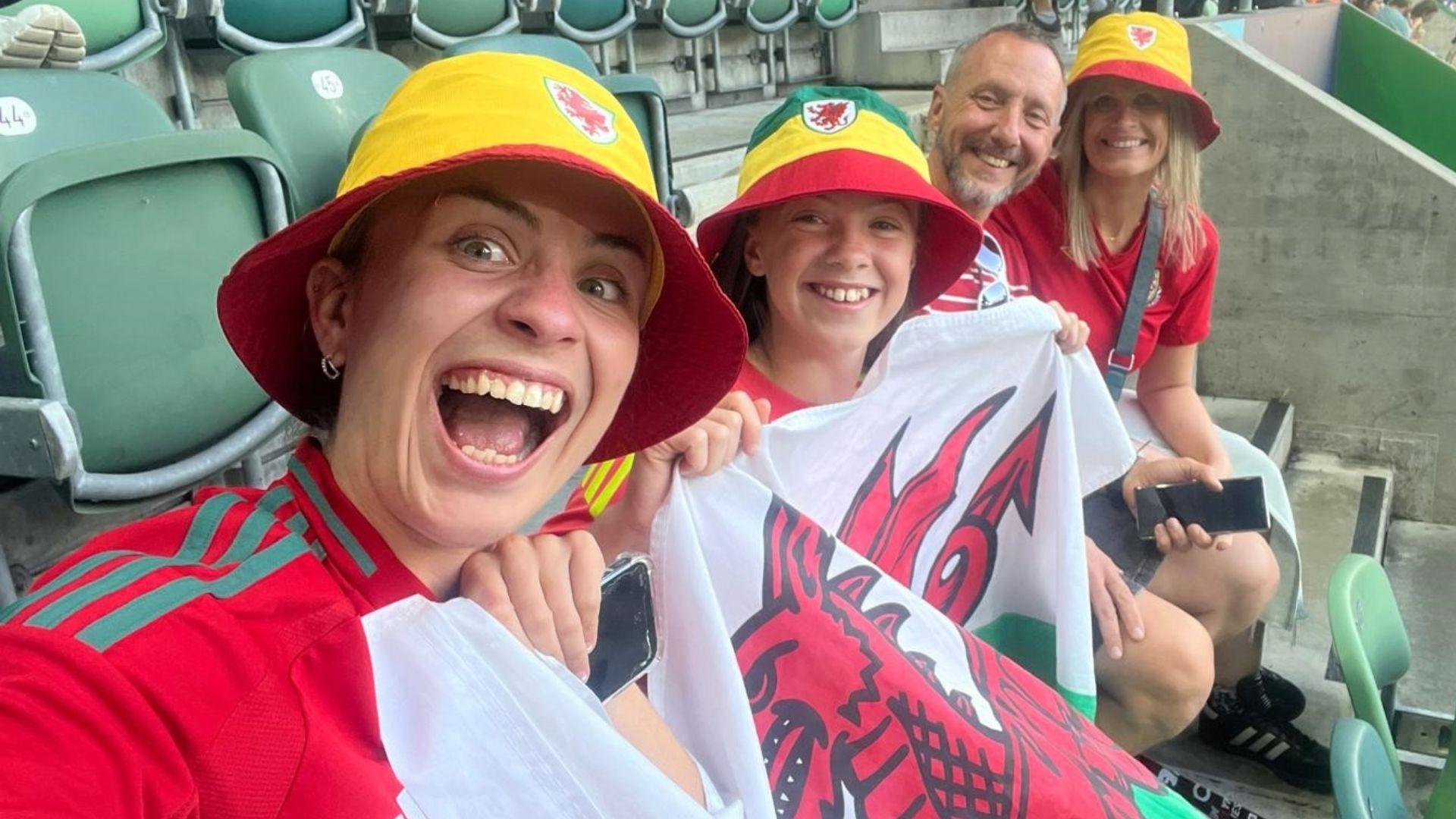 Llun o Mari (L) a'i chwaer Seren yn eistedd mewn stadiwm gyda'u rhieni. Mae Mari a Seren yn dal banner Cymru.