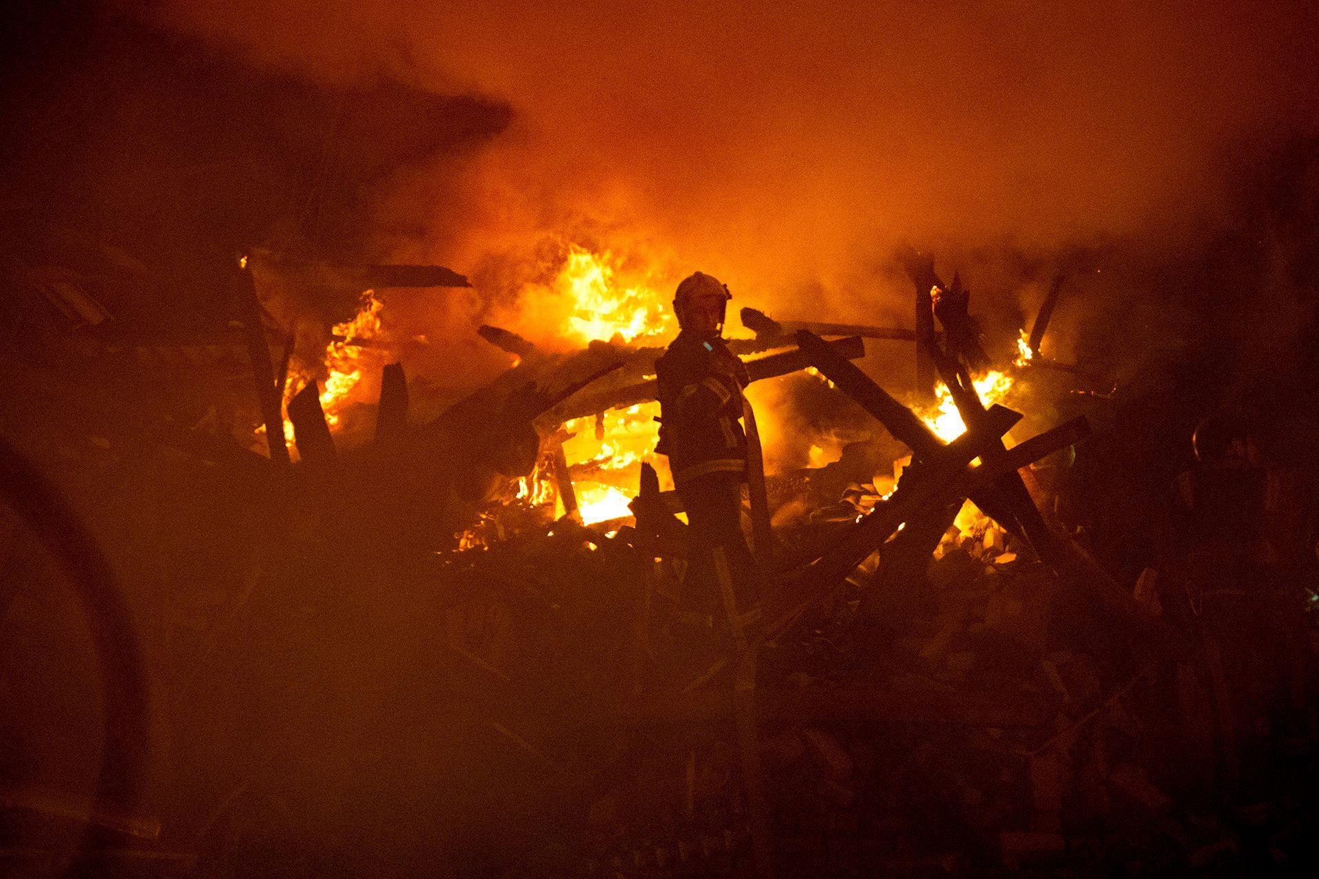 A firefighter is silhouetted against a raging fire amid debris of a building hit by a Russian missile strike and vignetted with darkness, in Sumy in October 2024.