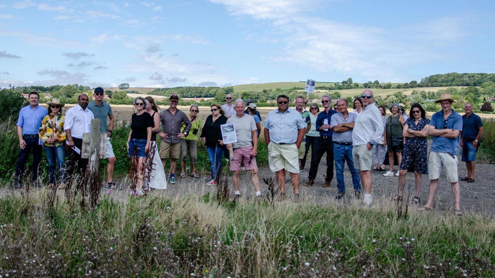 A group of around 20 poeple gathered in a field some holding placards