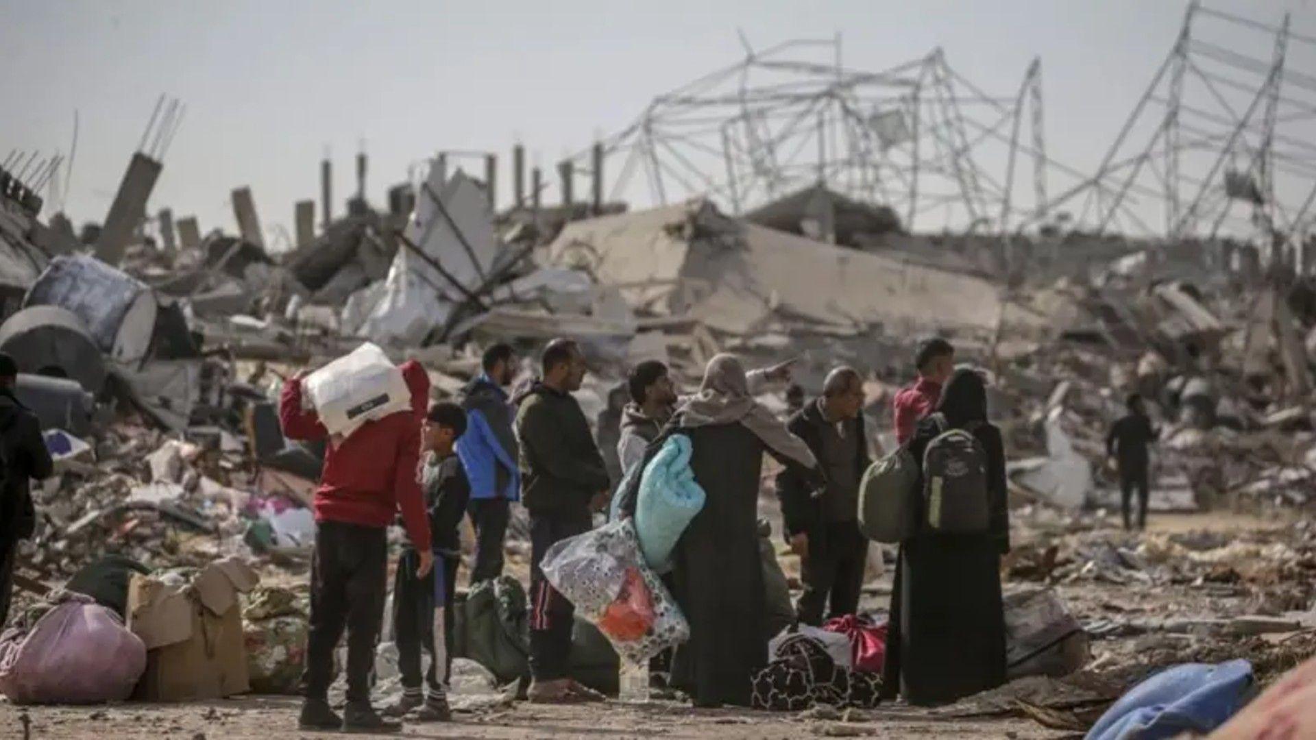 Group of Palestinians carrying luggage and surrounded by rubble as they return to Rafah