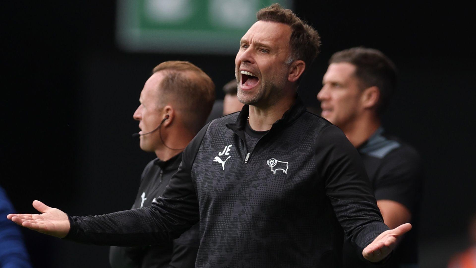 Derby County manager John Eustace opens mouth wide and shouts whilst holding his hands out wide. He wears a black Derby County quarter zip top