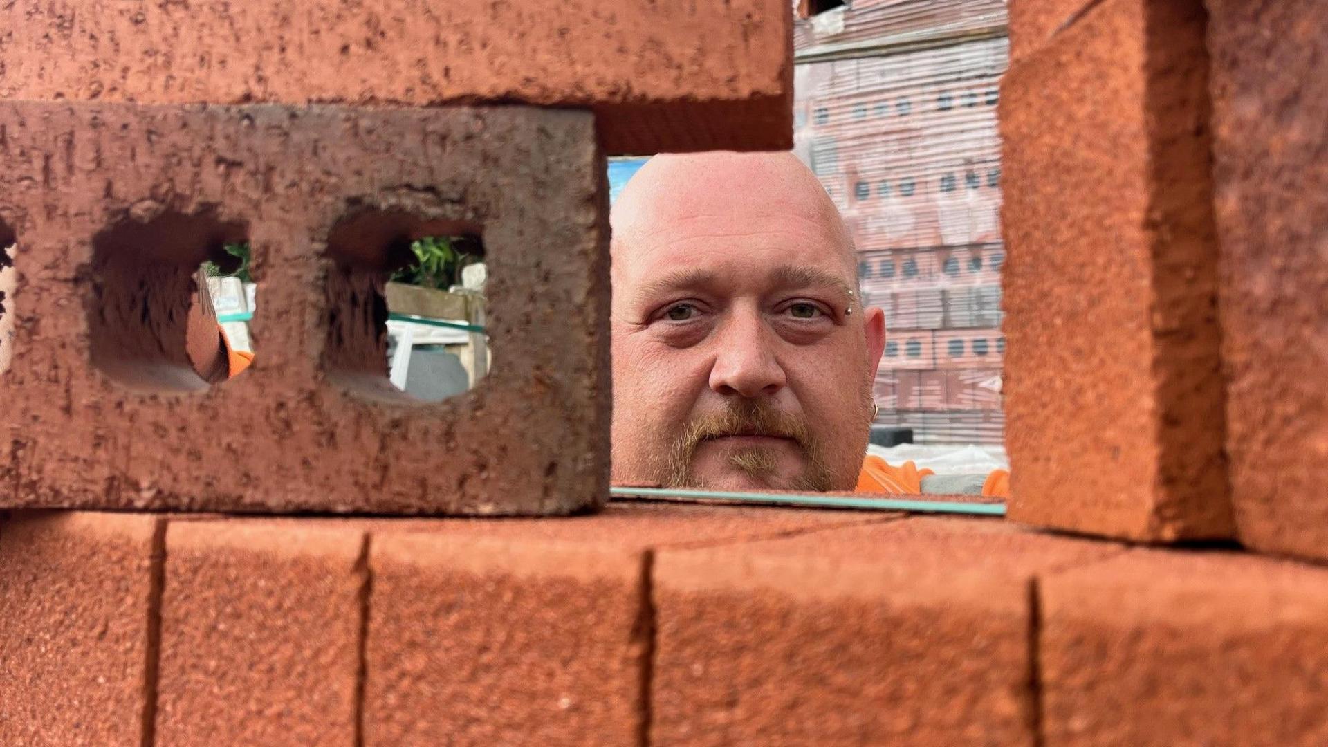 Delivery driver David Arnold poking his head through a red brick wall 