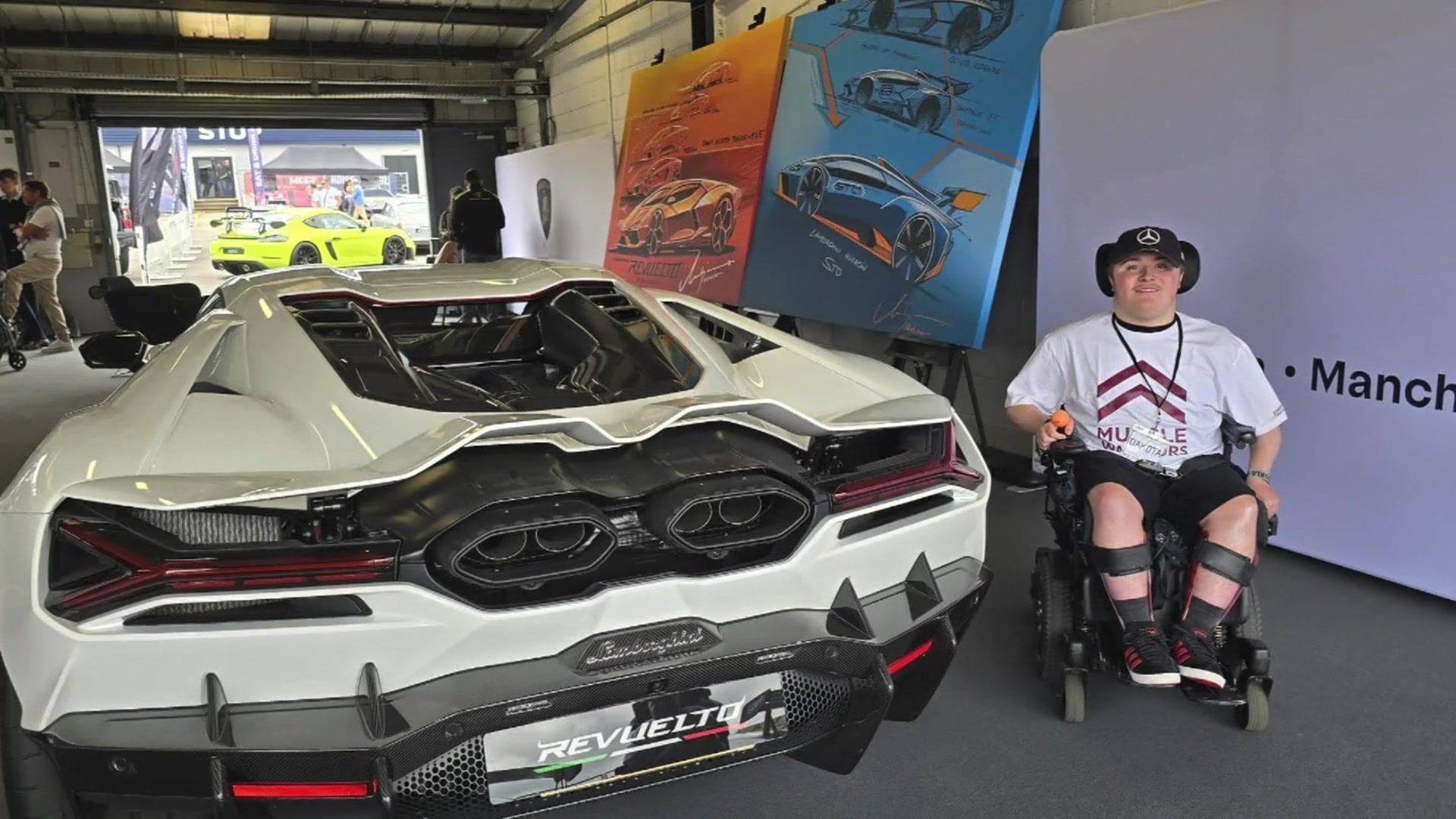 Dakota sitting in his chair next to a car in a museum 